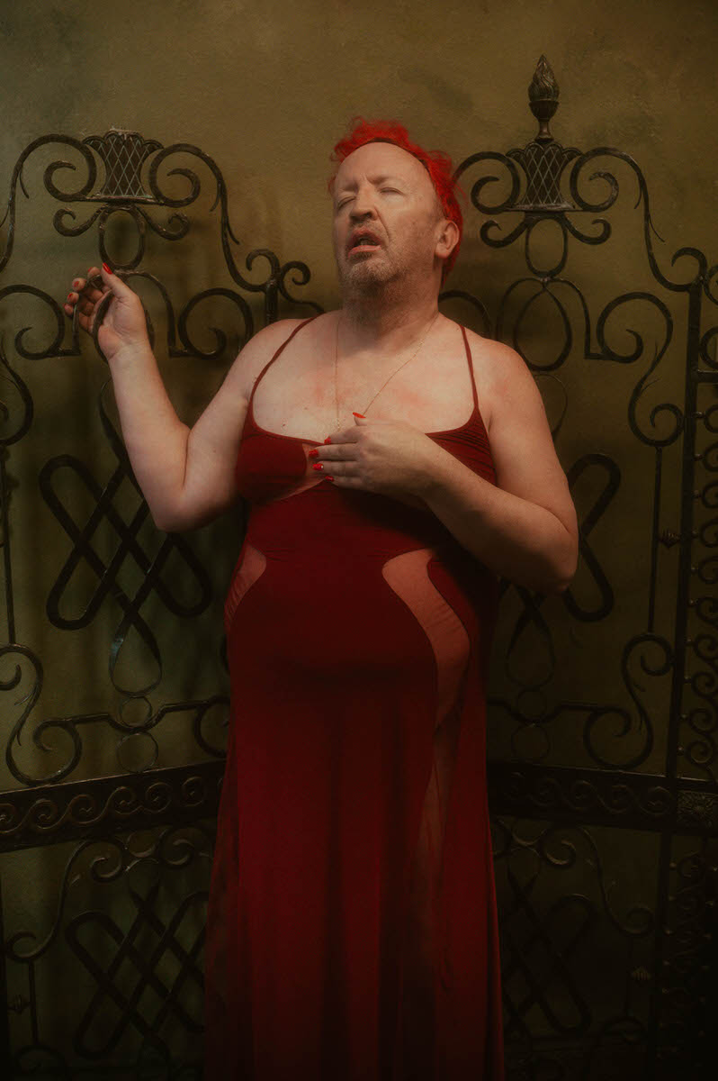 A man in a red dress posing for a boudoir session at a Dallas boudoir studio.