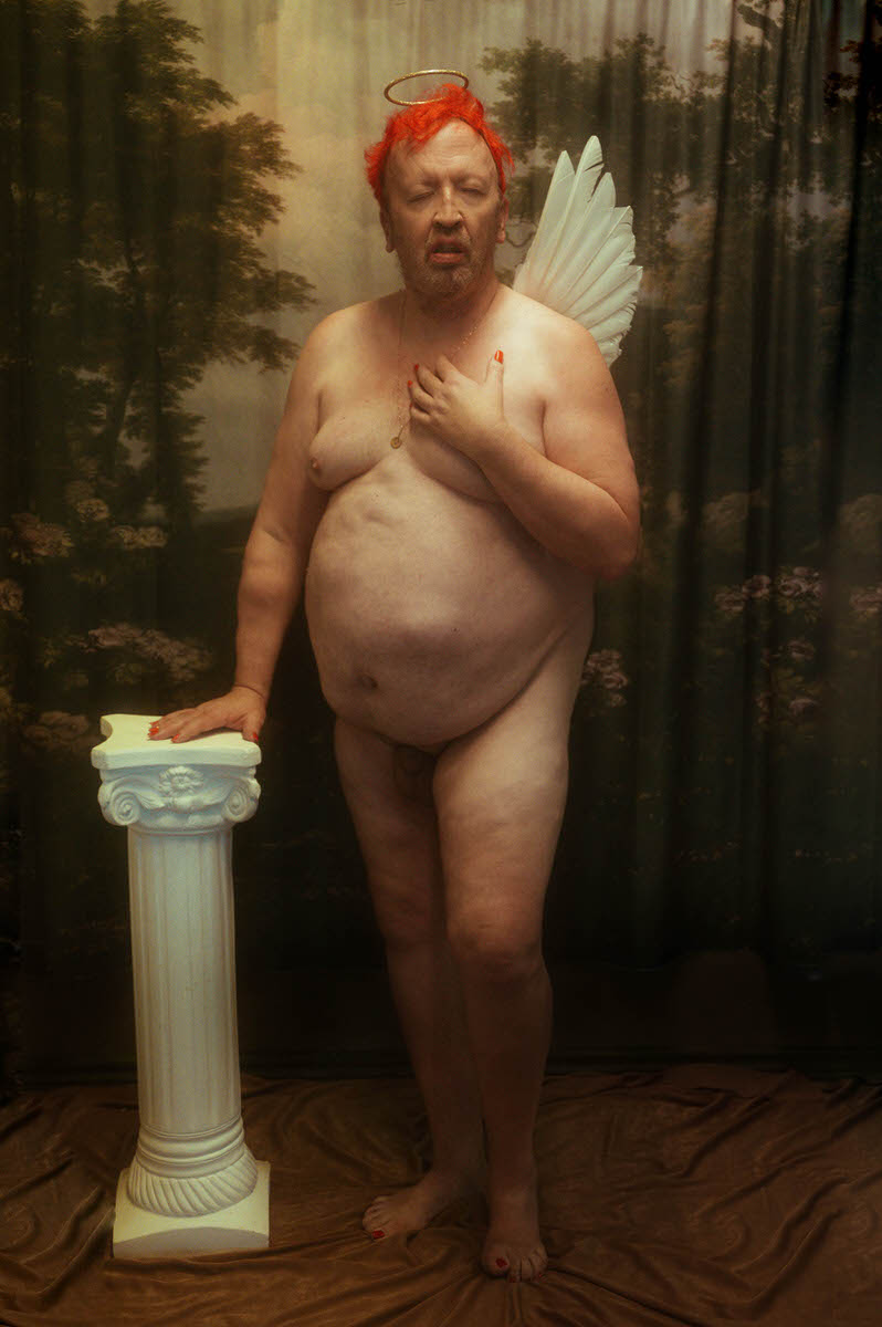 A trans woman wearing angel wings posing with a Greek pillar for a fine art boudoir photoshoot.
