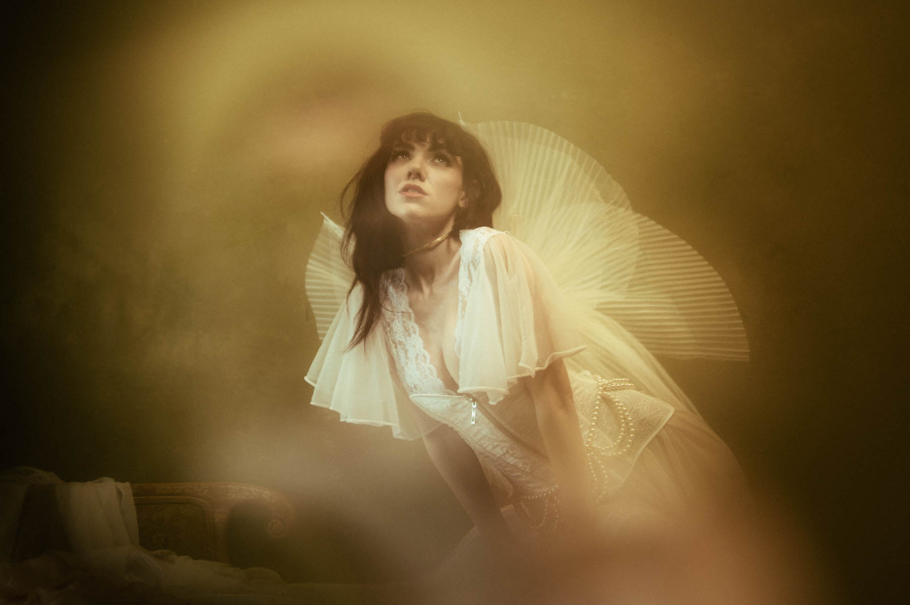 A woman in vintage clothing posing with angel wings in a hazy, dreamlike effect during a boudoir session.