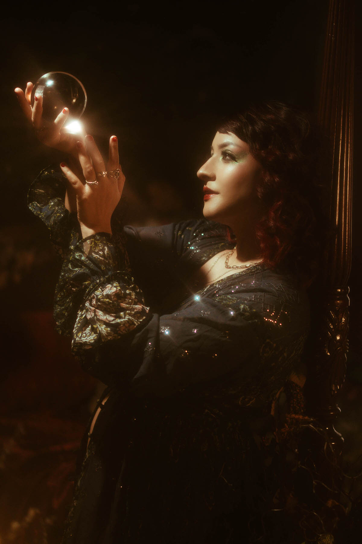 A cinematic maternity boudoir portrait featuring a mother-to-be in a dark, flowing gown, her figure softly illuminated by warm, moody lighting against an ornate, vintage backdrop.