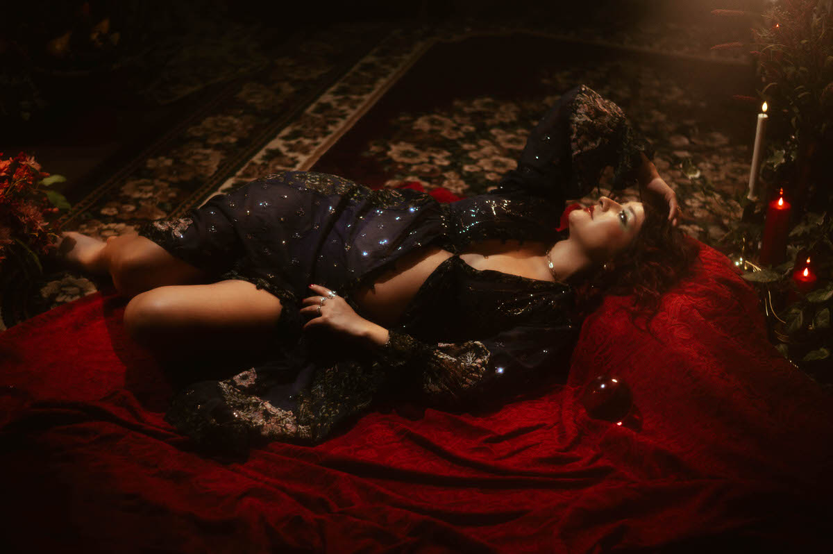 A timeless maternity portrait capturing the serene beauty of motherhood, with a mother-to-be in a sheer, detailed gown, laying on the ground, surrounded by soft, romantic lighting and antique decor.