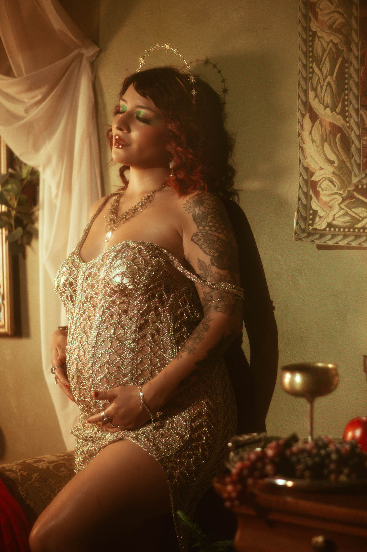 The subject stands with a confident, regal posture, her gold gown glowing in the warm, moody lighting. She gazes upward, hands gracefully holding a cluster of grapes, evoking the sensuality of classical sculpture.