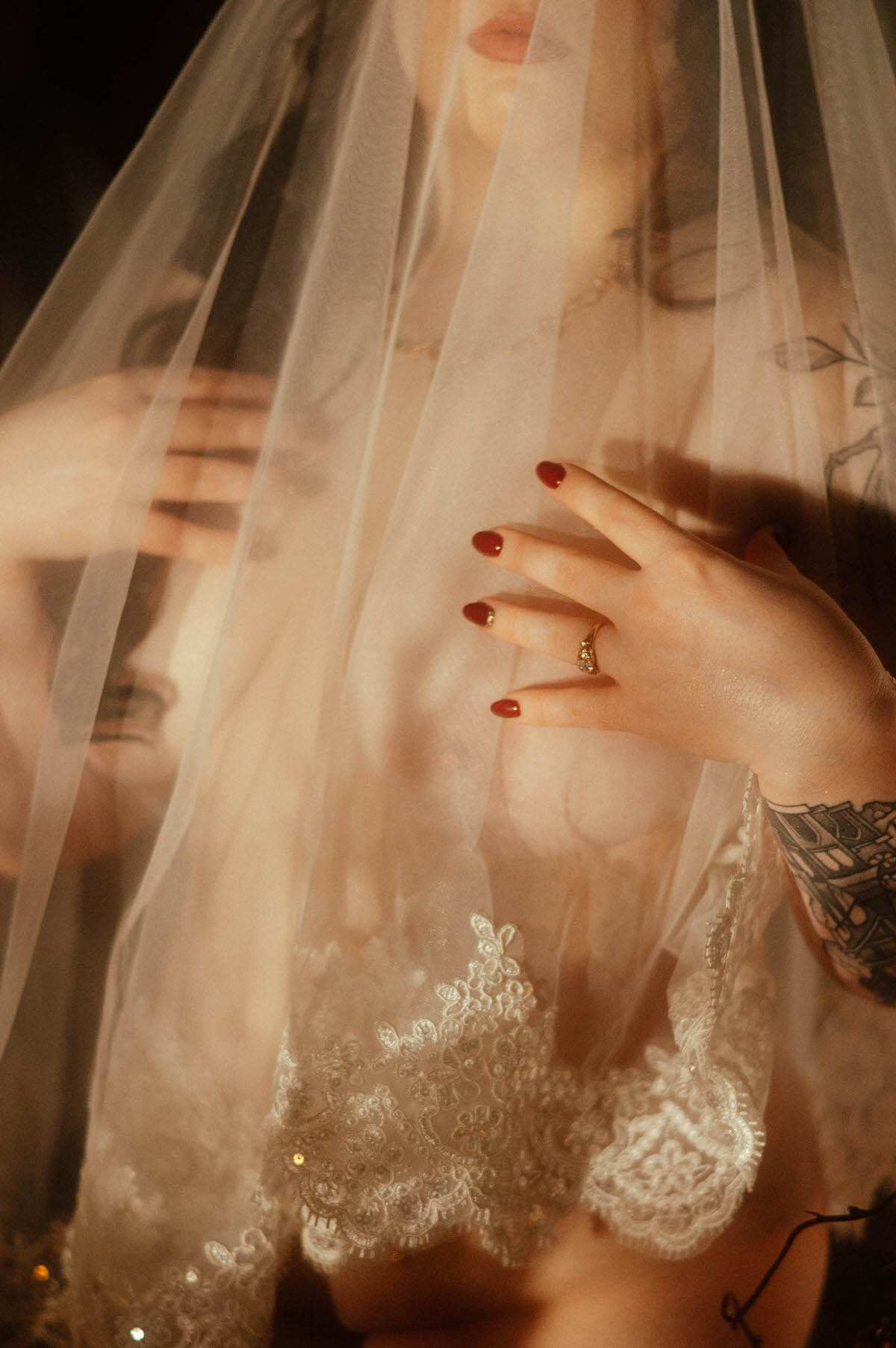 Close-up detail of a moody boudoir portrait featuring a sheer lace veil over the muse’s bare torso, with hands delicately posed and ruby red nails visible. The golden light and intricate embroidery evoke dreamy, artistic boudoir inspiration at Royal Lune Studio.