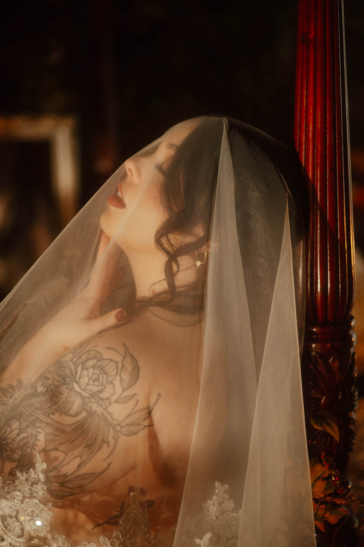 Romantic moody boudoir portrait of a tattooed muse beneath a delicate lace-trimmed veil, eyes closed in soft ecstasy, her hand resting on her neck. Shot at Royal Lune Studio, this image evokes cinematic lighting and intimate, creative boudoir inspiration.