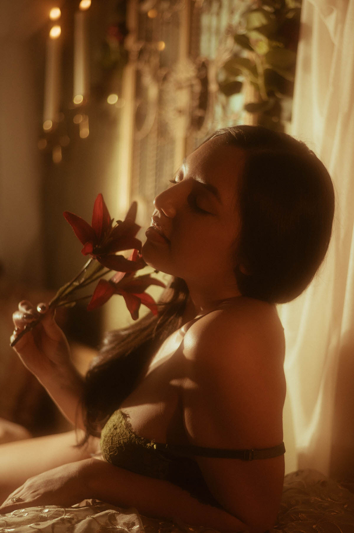 A client in profile holds a red lily near candlelight, captured in warm moody tones for an artistic nude photography session. This intimate boudoir image was created at a Dallas area studio. Royal Lune Photo.