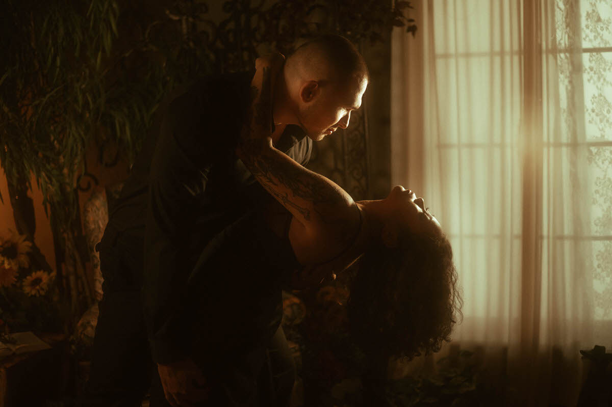 A couple shares an intimate dip pose during their romantic couples boudoir session at Royal Lune Studio, bathed in golden moody lighting near lace-draped windows. Their passionate connection and dramatic body language offer bold inspiration for moody couples boudoir and artistic couples boudoir poses.
