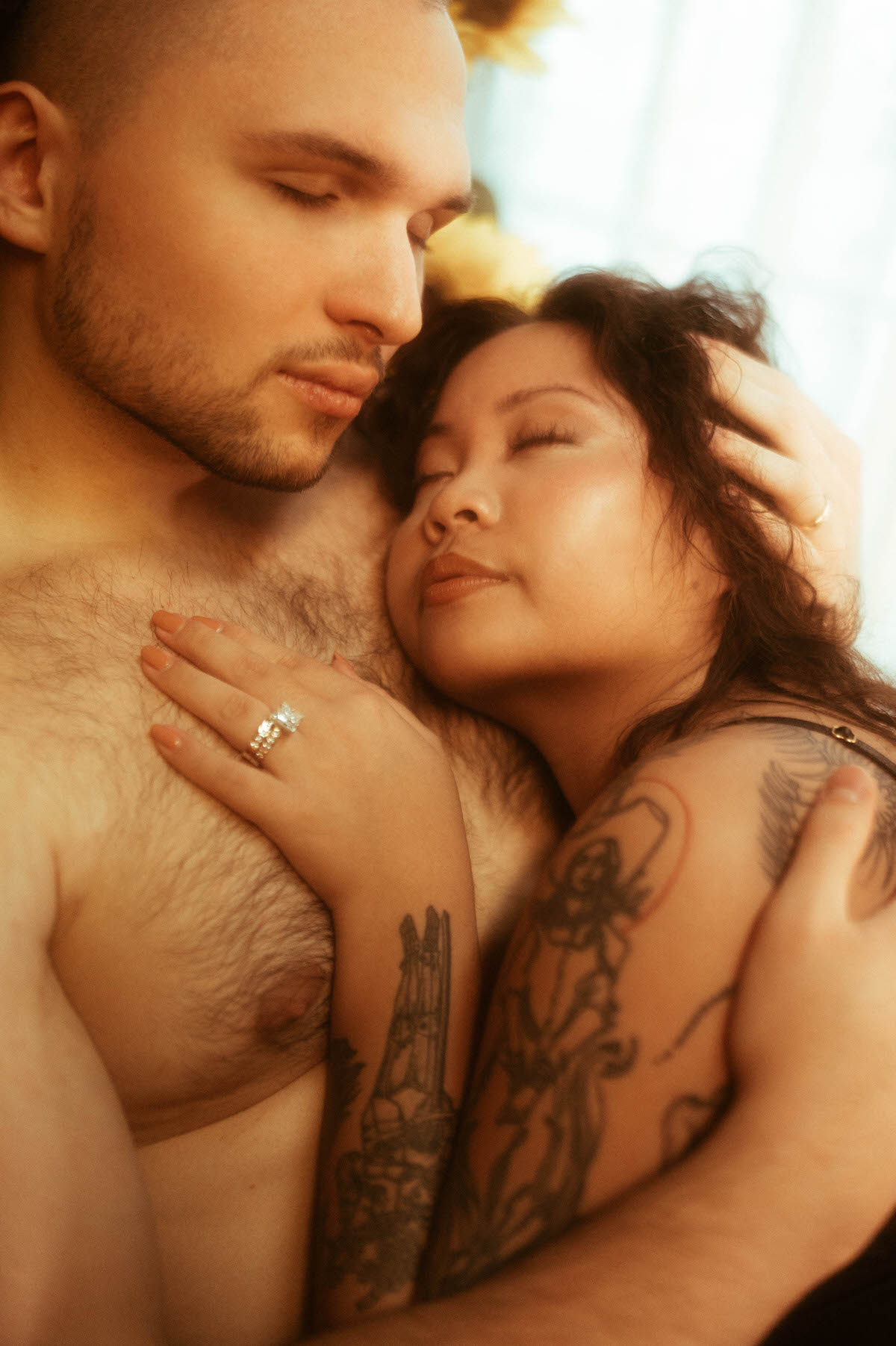 Close-up of a couple embracing with eyes closed, exuding tenderness and connection. The woman rests peacefully on her partner’s chest, framed by soft light and sunflower tones at Royal Lune Studio during a romantic couples boudoir photography session in Dallas.