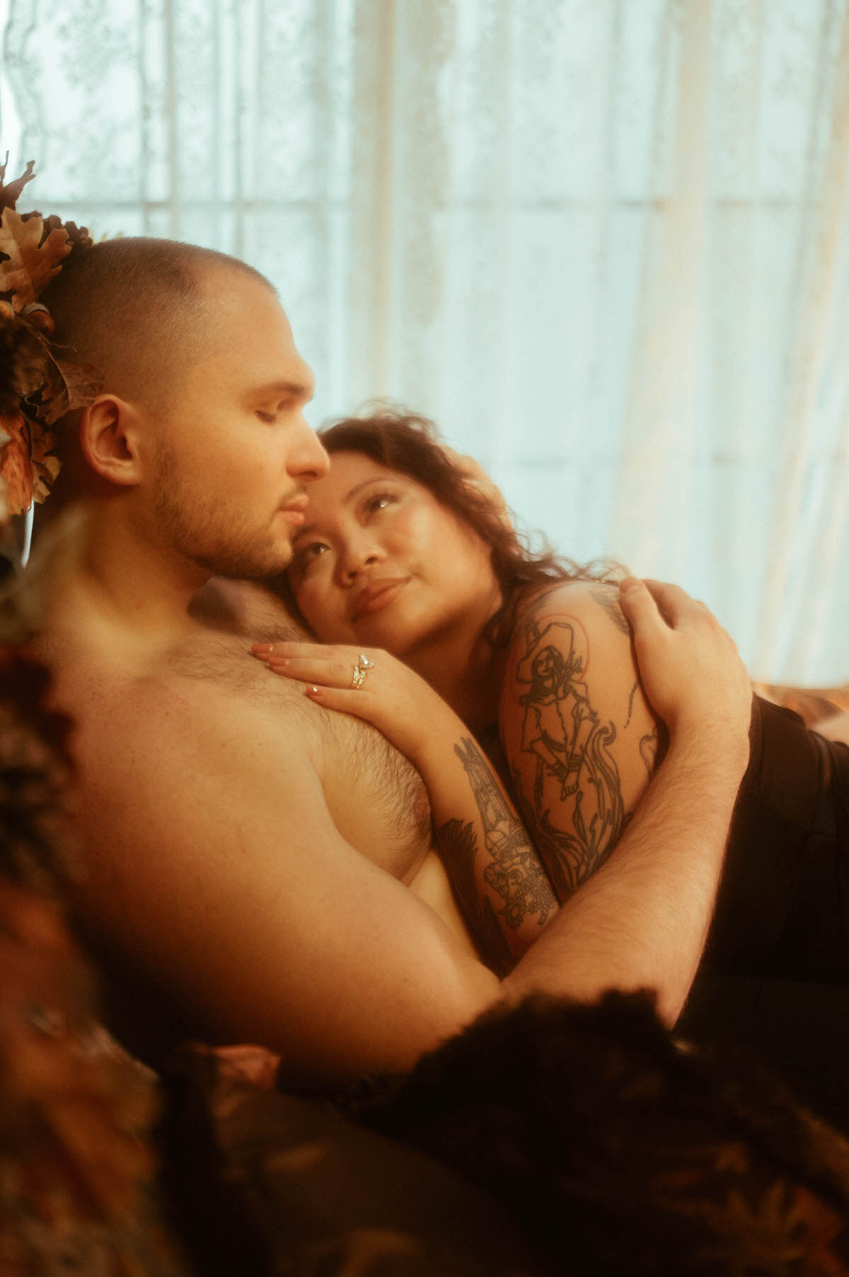 A woman in black lingerie rests her head on her partner’s bare chest, gazing up at him with adoration as he closes his eyes in calm intimacy. The soft lace curtains and autumnal tones at Royal Lune Studio create a dreamy, romantic setting for this Dallas romantic couples boudoir photography session.