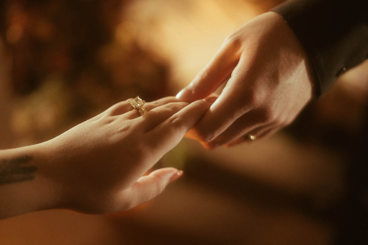 A close-up of two hands gently touching, with soft golden lighting illuminating an elegant engagement ring. This romantic couples boudoir detail shot captures the intimacy and connection between partners, perfect for a moody couples boudoir or spicy couple photoshoot at Royal Lune Studio.