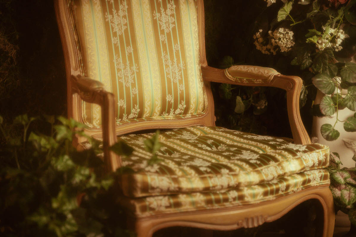 Close-up of a vintage French Louis XVI armchair with gold and green floral upholstery at Royal Lune Studio, part of a whimsical Dallas boudoir studio setup for spring photography sessions.