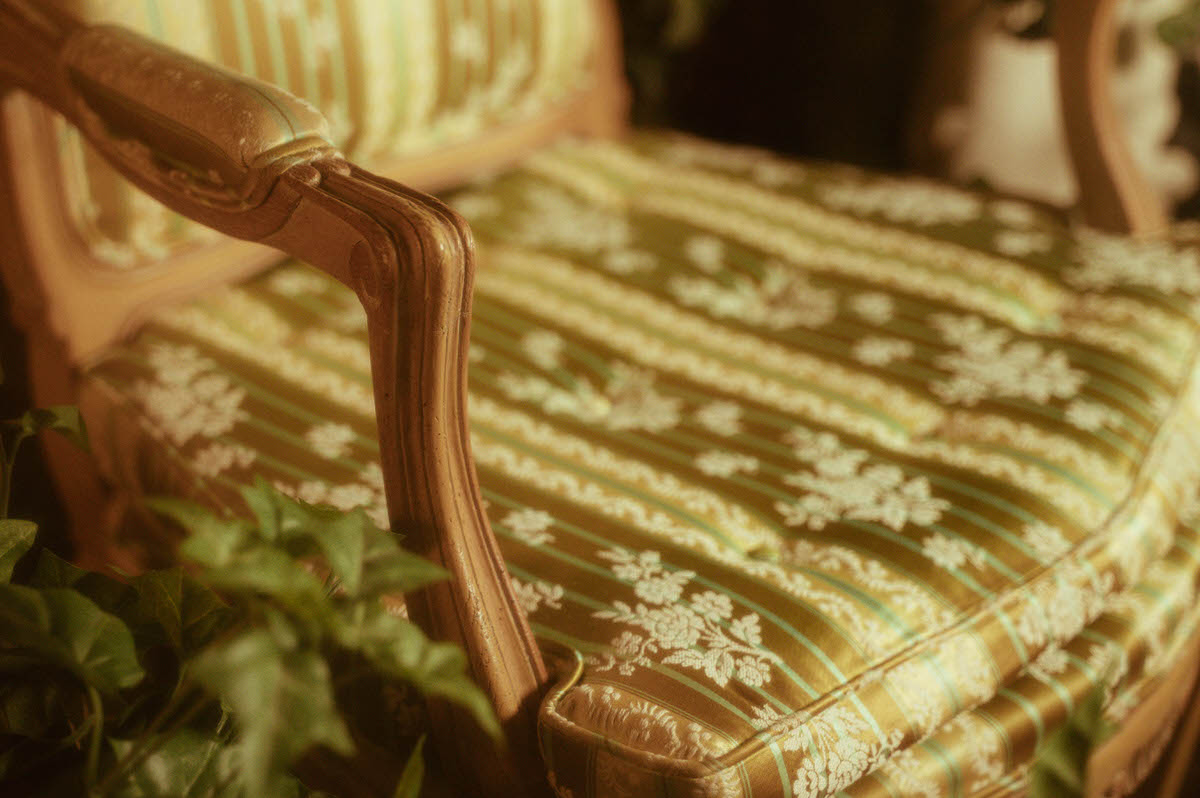 Detail shot of the carved wood armrest and brocade cushion of a vintage French Louis XVI chair, part of the elegant boudoir studio setup at Royal Lune Studio, a Dallas boudoir studio and spring photography location.