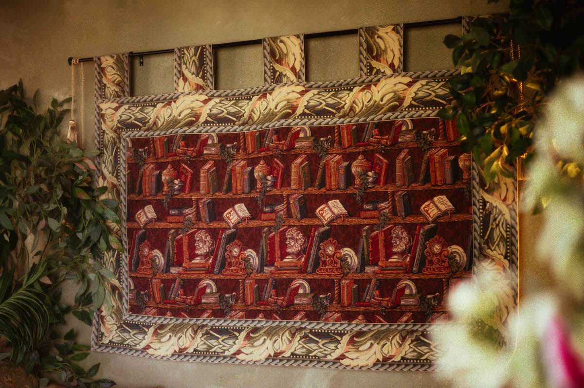 Decorative bookshelf tapestry with rich red and gold tones, framed by silk greenery on the wall at Royal Lune Studio, adding a vintage academic flair to the spring Dallas boudoir studio setup.