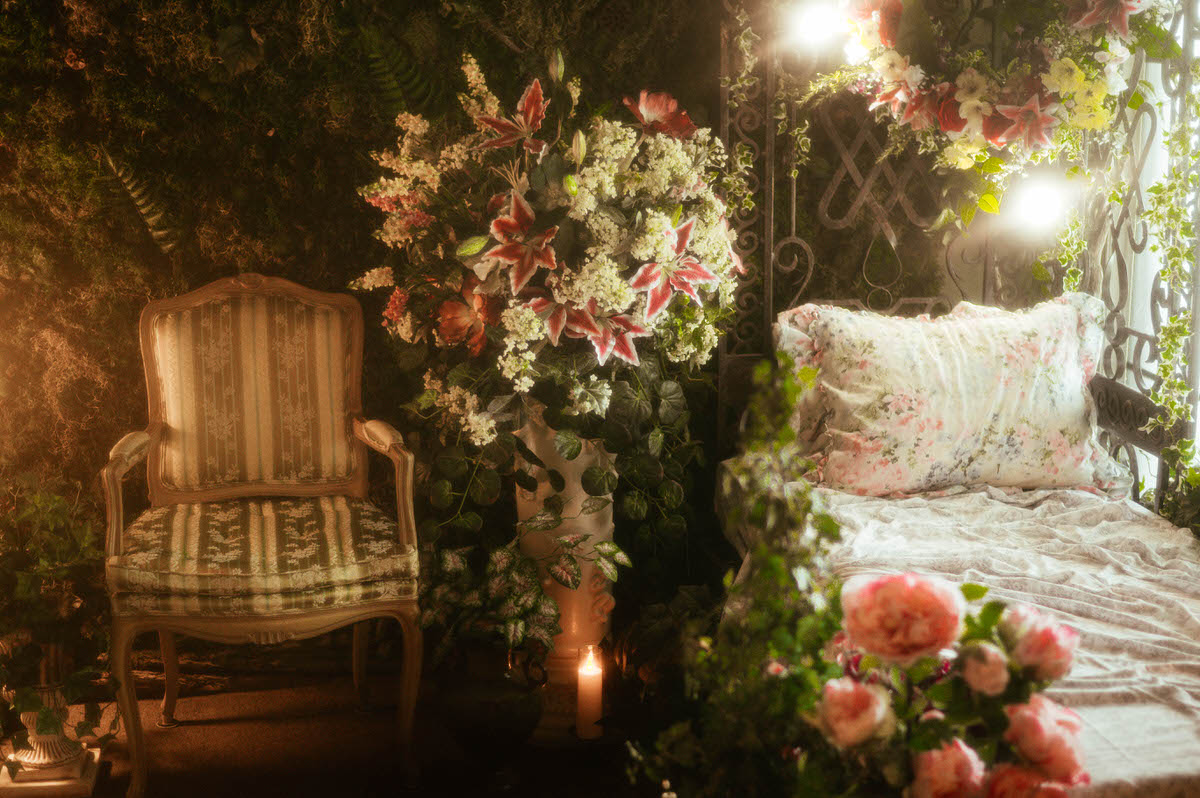 Romantic spring studio setup at Royal Lune Studio featuring an antique French Louis XVI armchair, vintage iron daybed with floral bedding, and silk florals beneath a moss wall—perfect for dreamy sessions at this Dallas boudoir studio and Dallas photography studio for rent.