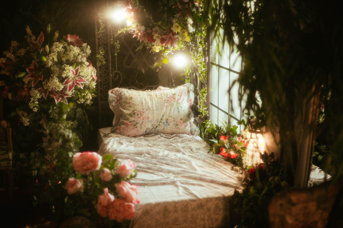 Romantic floral bed setup at Royal Lune Studio with sheer white draping, ivy vines, glowing lights, and a flower-covered wrought iron frame—ideal for spring photography studio setups and Dallas boudoir sessions.