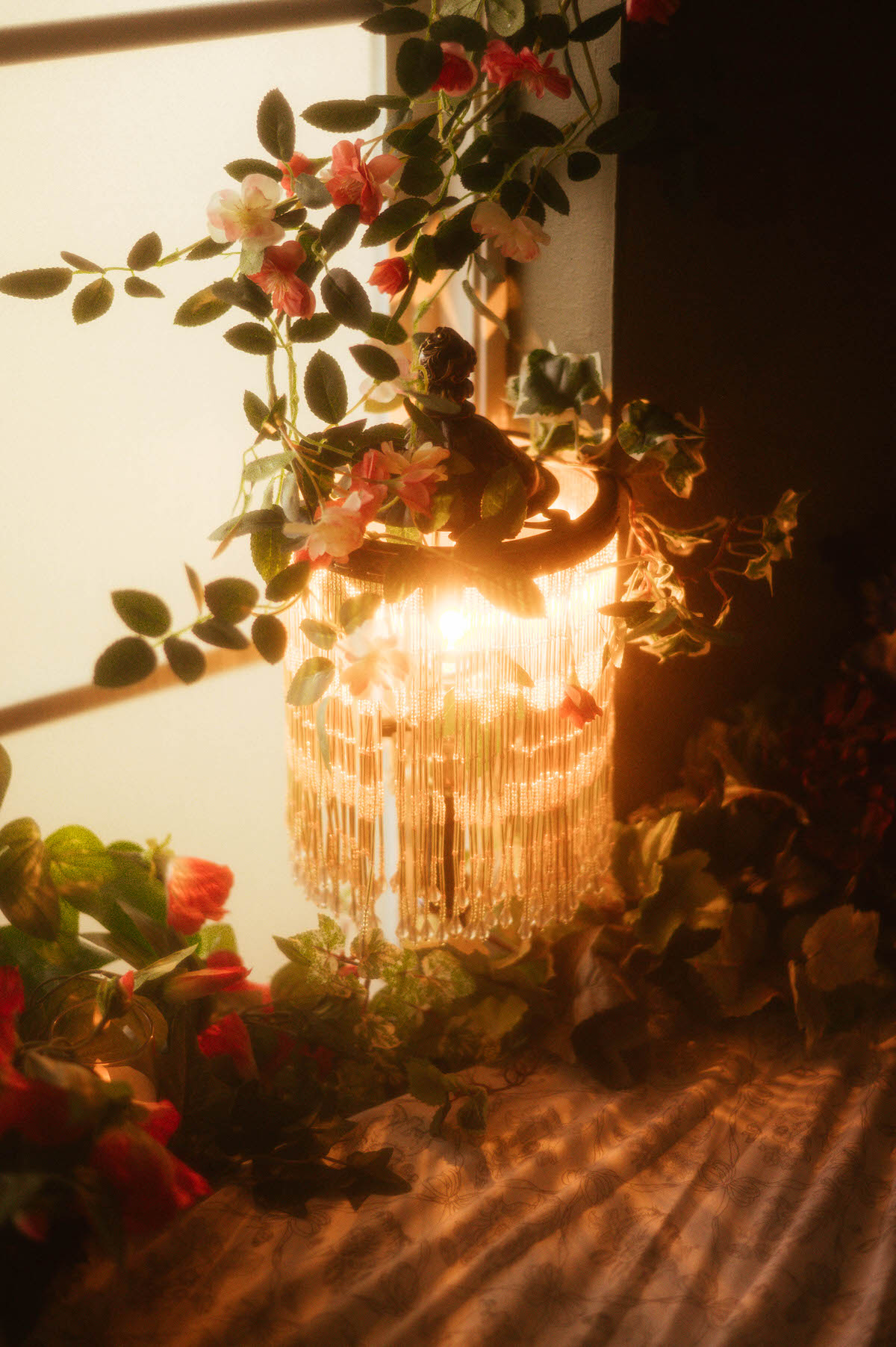 Vintage beaded lamp glowing warmly beside a daybed at Royal Lune Studio, adorned with trailing vines and pink silk flowers—part of a spring-inspired Dallas boudoir studio setup.