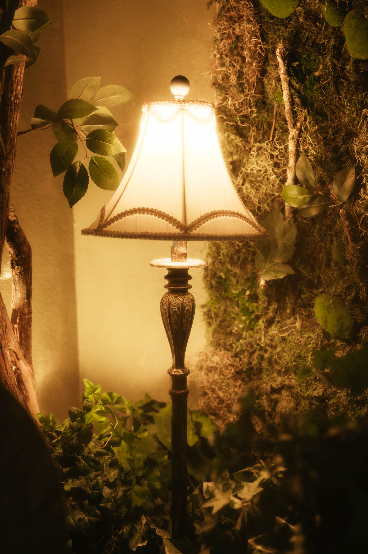 Vintage lamp glowing softly beside the moss wall installation at Royal Lune Studio, surrounded by faux ivy and branches, enhancing the romantic spring photography studio setup in this Dallas boudoir studio and photo studio rental.