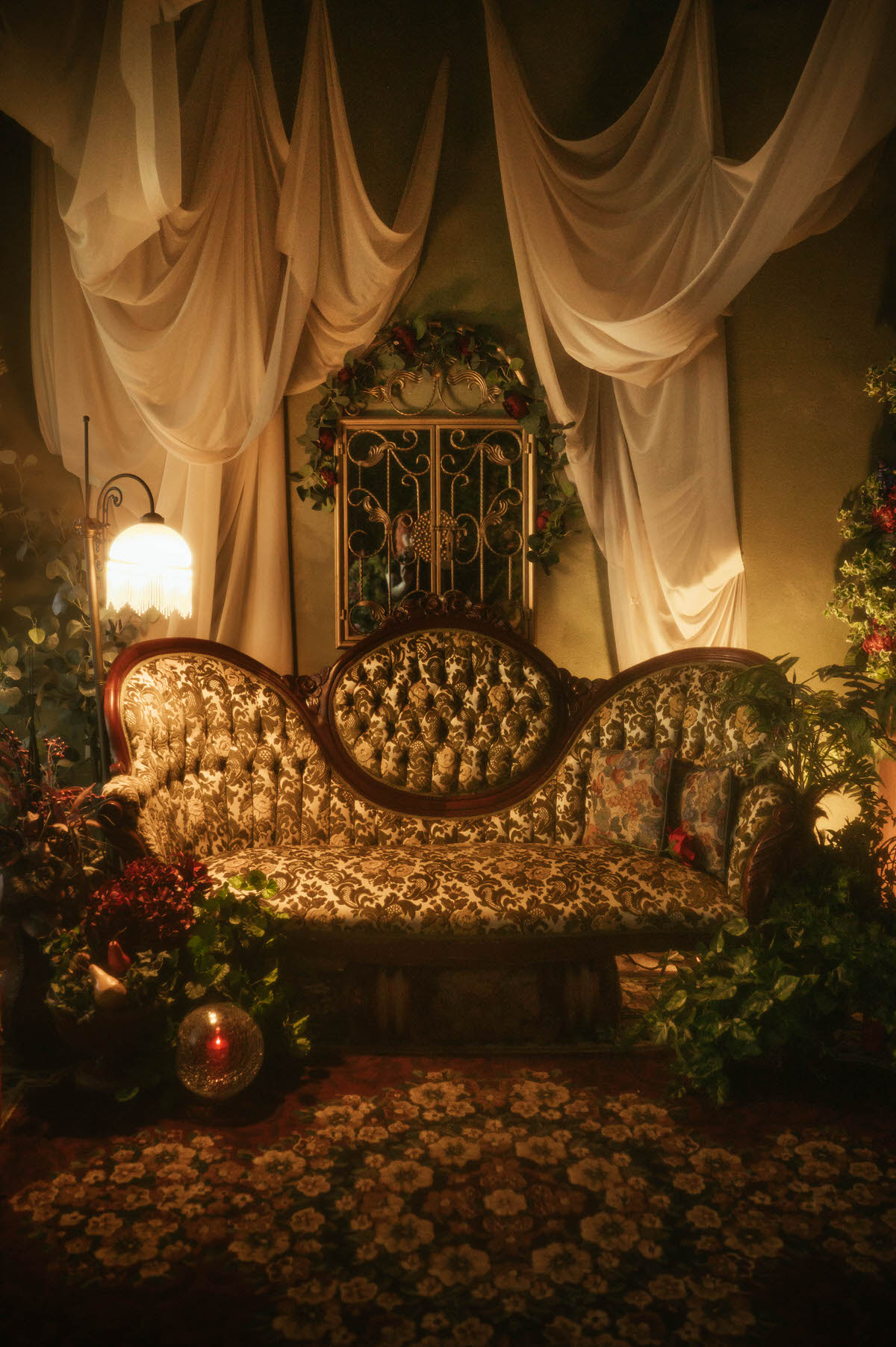 Full view of Royal Lune Studio’s spring boudoir setup featuring a velvet Victorian-style sofa, antique fringe floor lamp, romantic draped fabric ceiling, and gold scrollwork window, surrounded by greenery and vintage floral pillows for a dreamy Dallas boudoir studio scene.