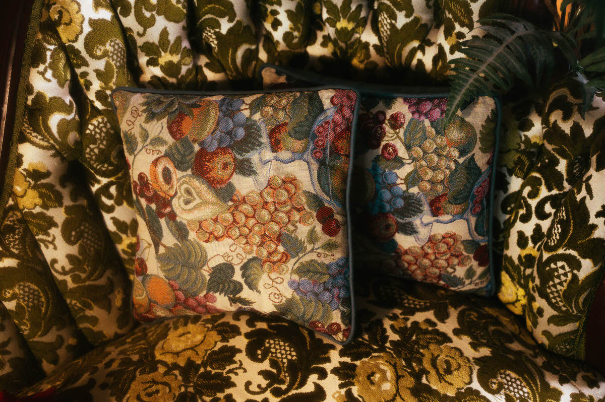 Close-up of vintage fruit tapestry pillows resting on a tufted Victorian sofa at Royal Lune Studio, showcasing ornate textures and rich, moody tones in this spring-inspired Dallas boudoir studio setup.