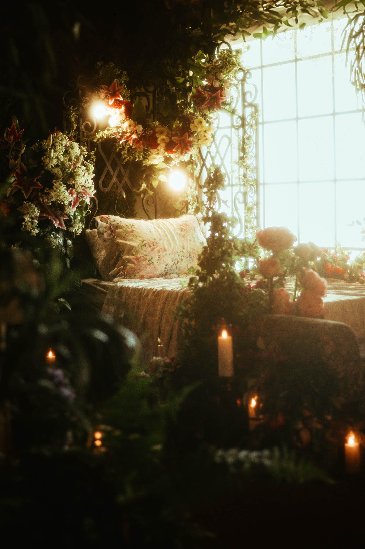 Romantic boudoir bed setup at Royal Lune Studio, surrounded by silk florals, candles, and greenery with soft natural light pouring through a large window, perfect for spring photography studio setup in a Dallas boudoir studio.