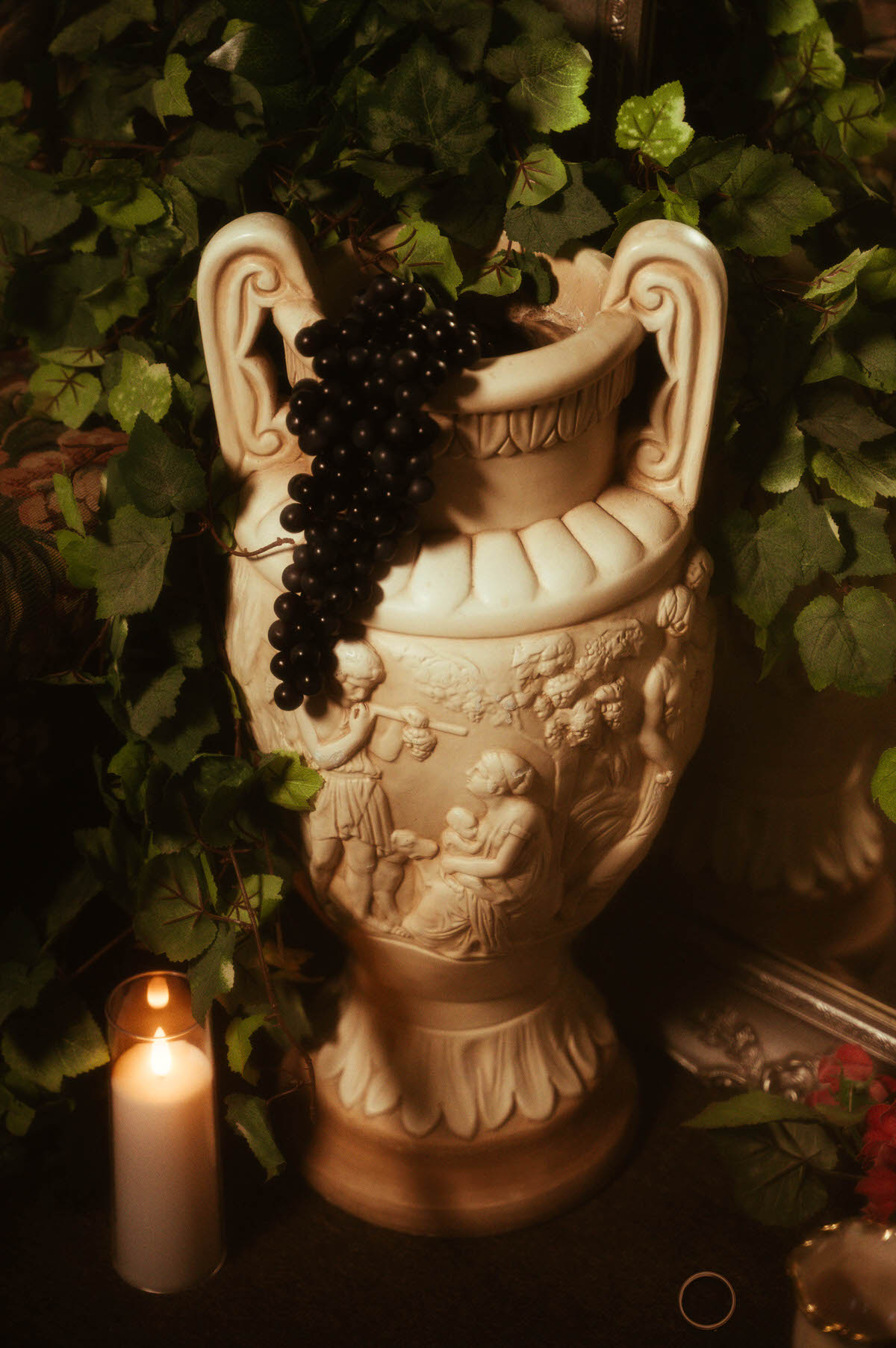 Ornate Grecian-style ceramic urn adorned with faux black grapes and surrounded by ivy vines and candlelight at Royal Lune Studio, creating a romantic vignette for a Dallas boudoir studio scene.