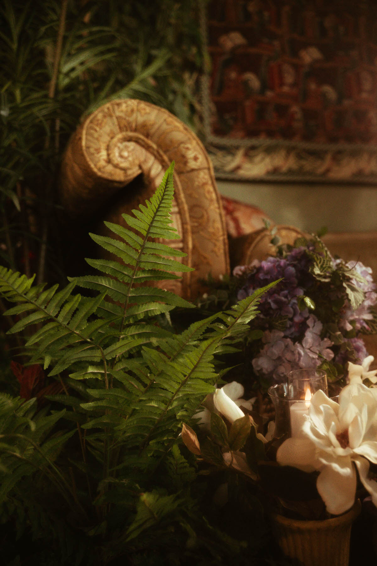 Vintage tapestry lounge chair surrounded by ferns, silk florals, and soft candlelight at Royal Lune Studio, showcasing the romantic spring boudoir studio setup in this Dallas photography space.
