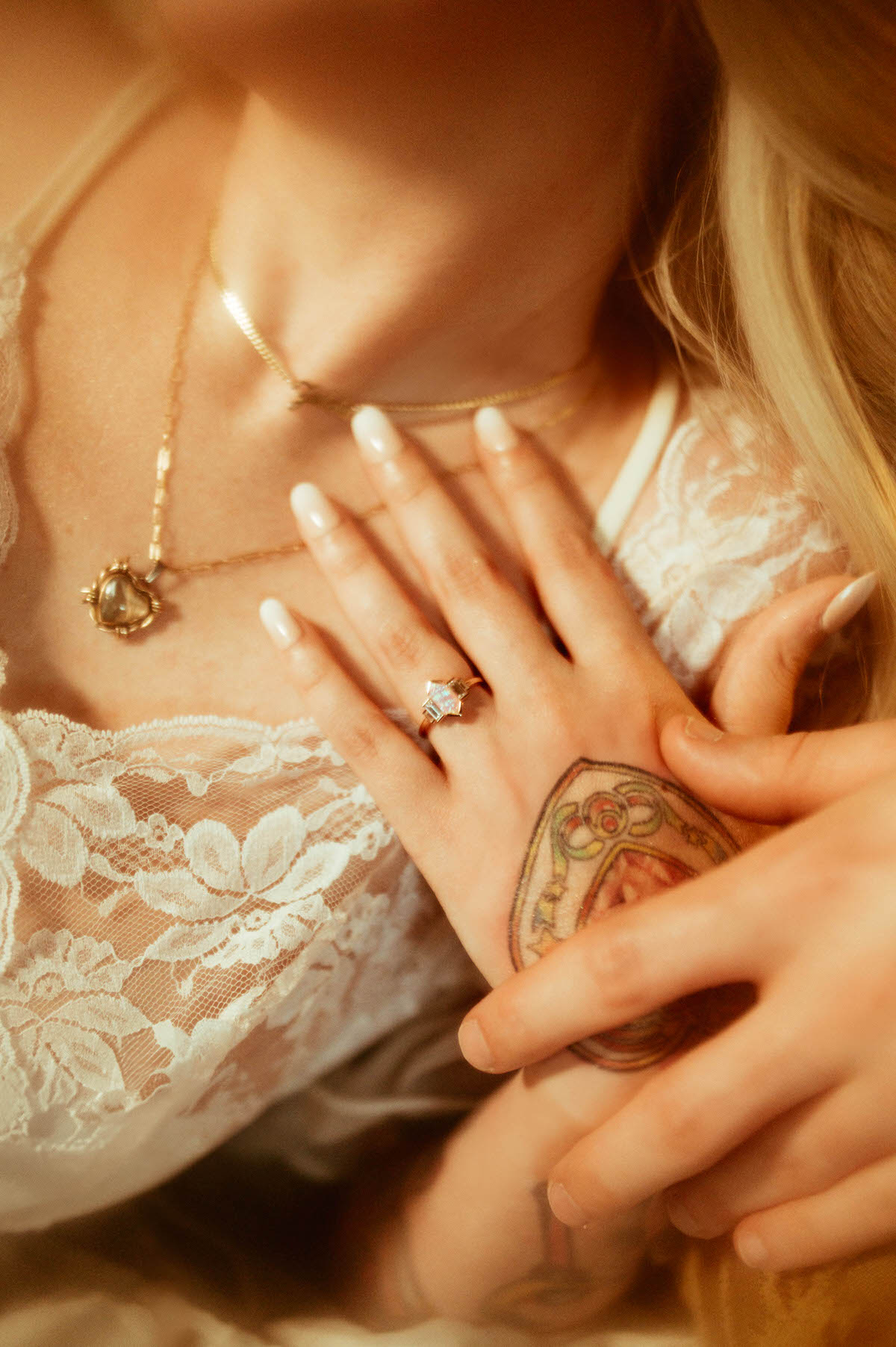 Close-up of the couple’s hands as the woman gently rests her hand over her partner’s, showcasing a radiant gemstone engagement ring and lace bridal lingerie. Shot at Royal Lune Studio, this romantic Dallas engagement photo highlights delicate jewelry, soft lighting, and tender connection.