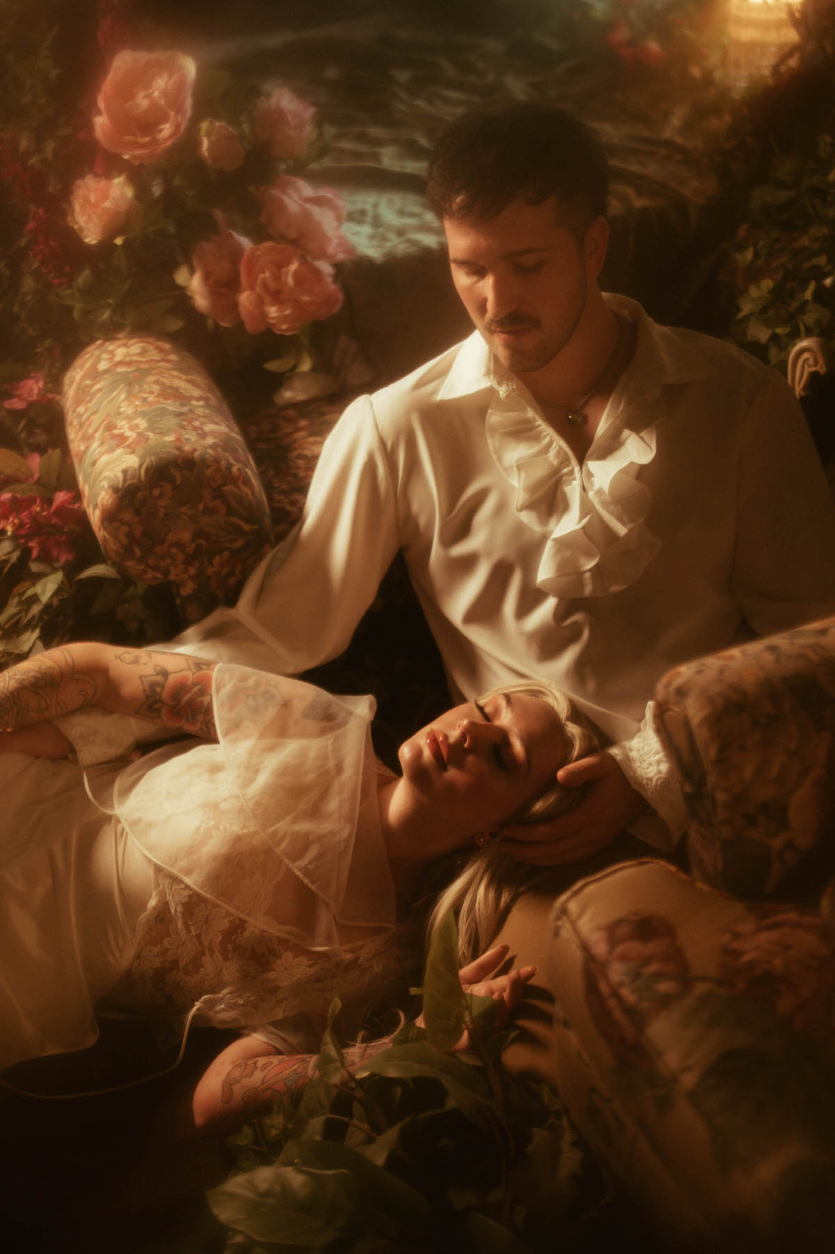 Whimsical engagement photo at Royal Lune Studio, featuring a romantic moment where the woman lies across the man's lap with her eyes closed, surrounded by antique floral furniture and soft golden lighting. The dreamy setting highlights vintage styling and intimate connection.