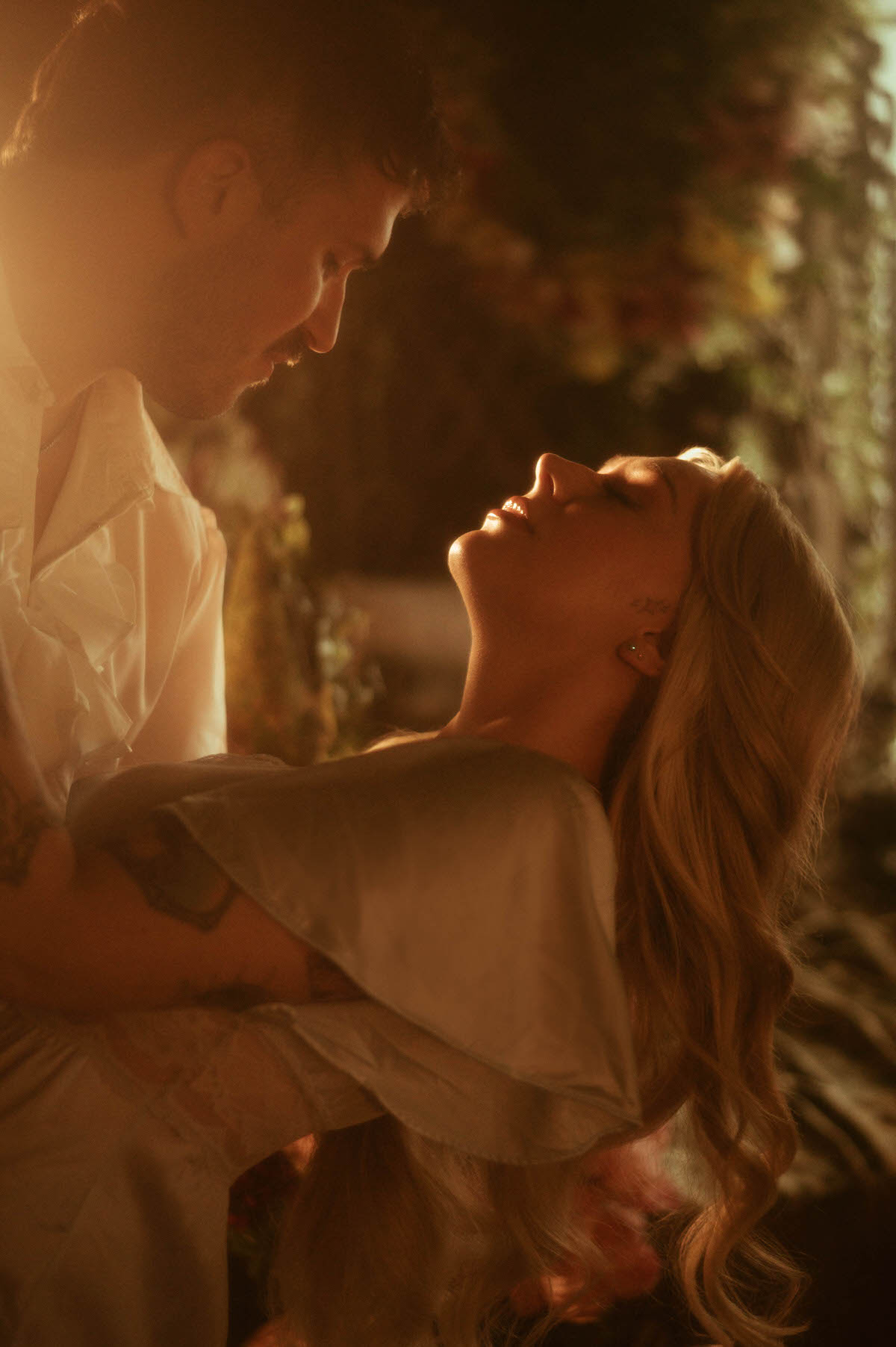A romantic engagement moment at Royal Lune Studio as the couple leans in close, the woman arching gracefully in the man's arms beneath soft golden lighting. Her long waves and satin sleeve catch the glow, creating a dreamy, intimate atmosphere.