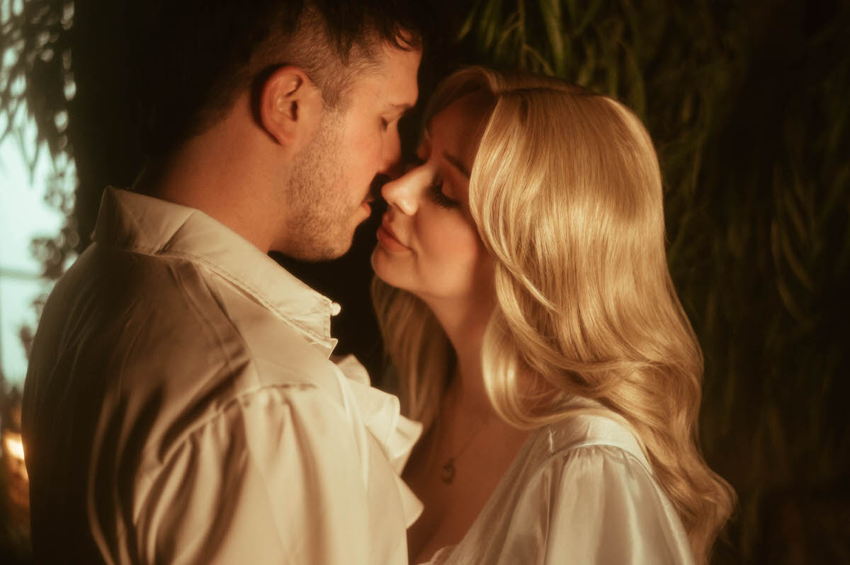 A close-up of a couple leaning in for a kiss at Royal Lune Studio, bathed in warm golden light, with soft vintage styling and greenery creating a dreamy, romantic atmosphere.