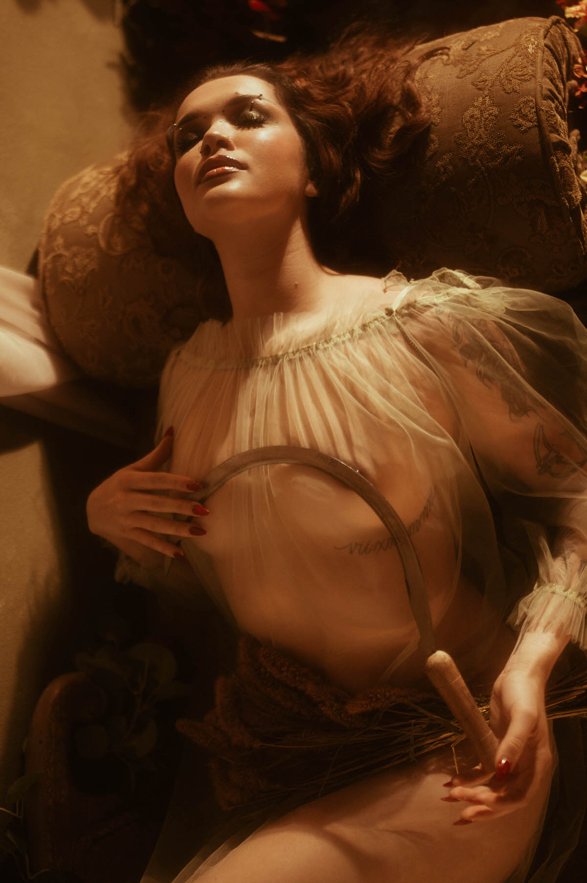 A fall photoshoot inspiration close up shows a woman reclining with a sickle held to her chest beneath sheer tulle, drawing from the painting Allegory of Summer. Royal Lune Photo