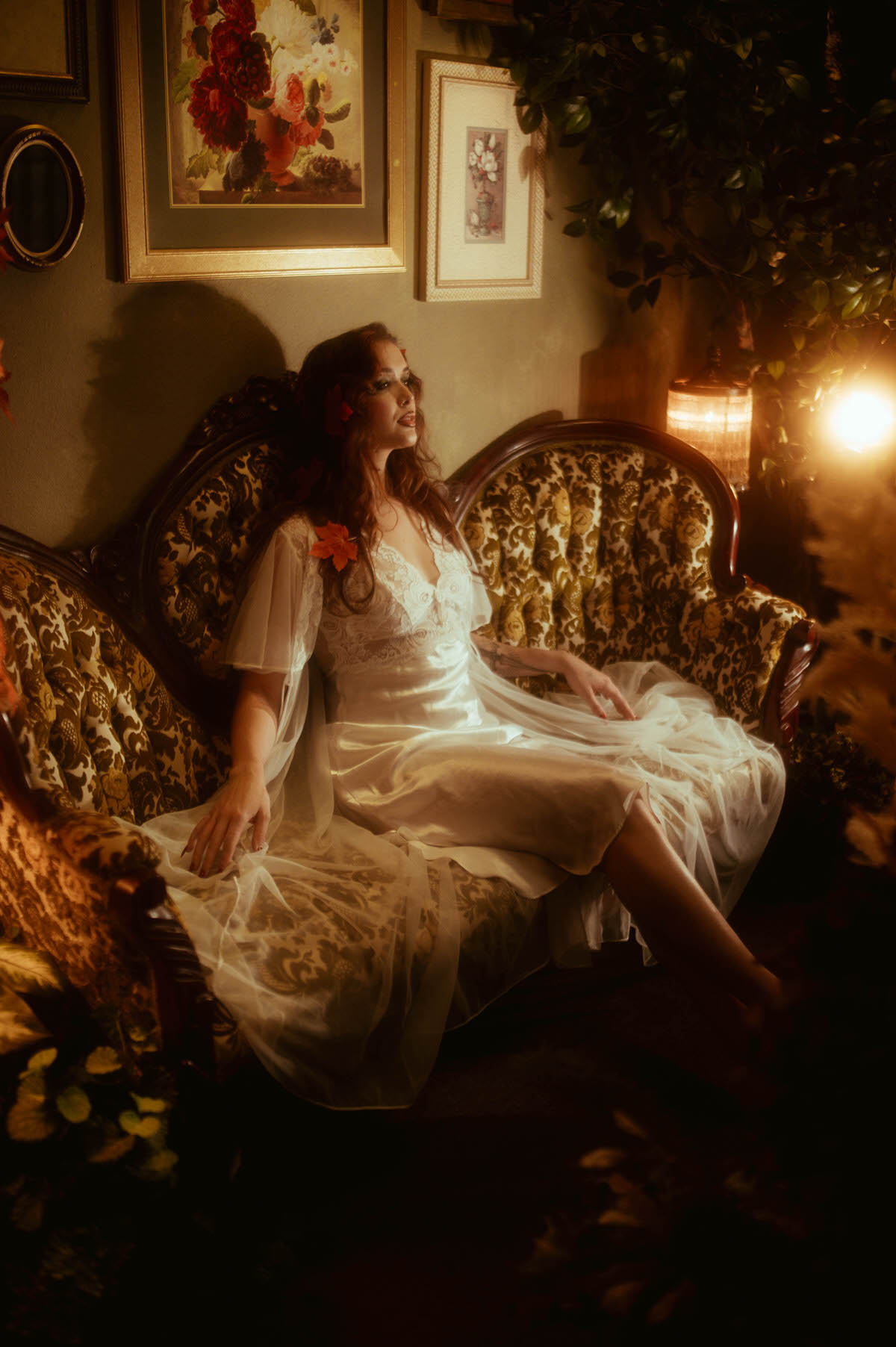 Dreamy autumn photography frames a woman in ivory satin lounging beside a glowing lantern and trailing greenery, her expression wistful and serene. Royal Lune Photo.