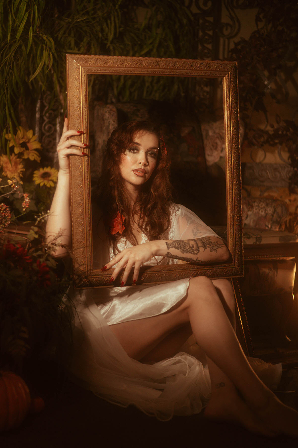 A fall boudoir photoshoot portrait frames a woman in white lace through an ornate gold mirror, surrounded by sunflowers and autumn greenery. Royal Lune Photo.