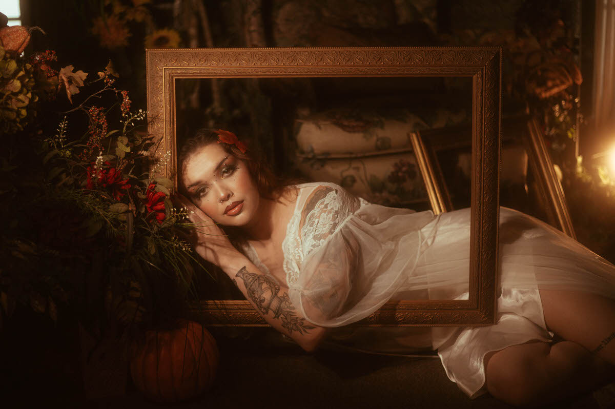 Dreamy autumn photography shows a woman in a flowing white slip resting her head against a gold picture frame near pumpkins and wildflowers. Royal Lune Photo.