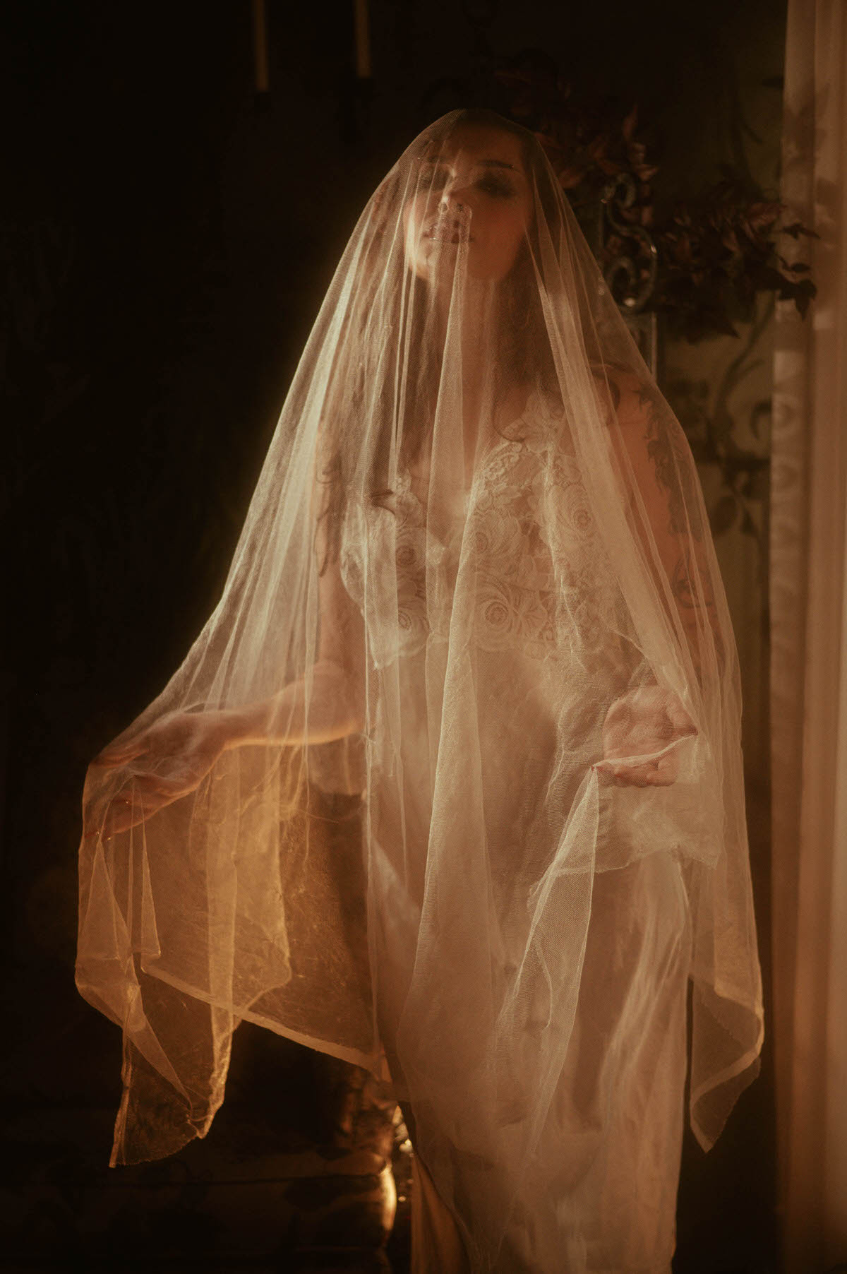 A fall boudoir photoshoot silhouette features a woman draped in sheer veiling with her arms spread wide as golden light filters through the fabric. Royal Lune Photo.