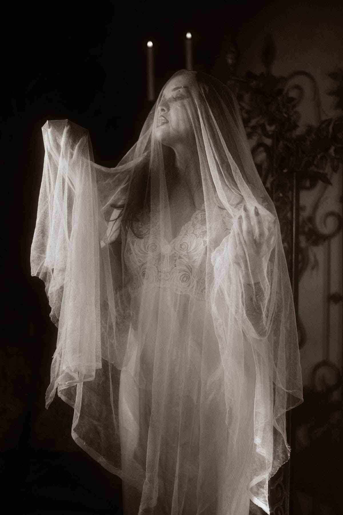A moody fall photos black and white portrait captures a woman shrouded in sheer veiling with her face tilted upward and candles glowing behind her. Royal Lune Photo.