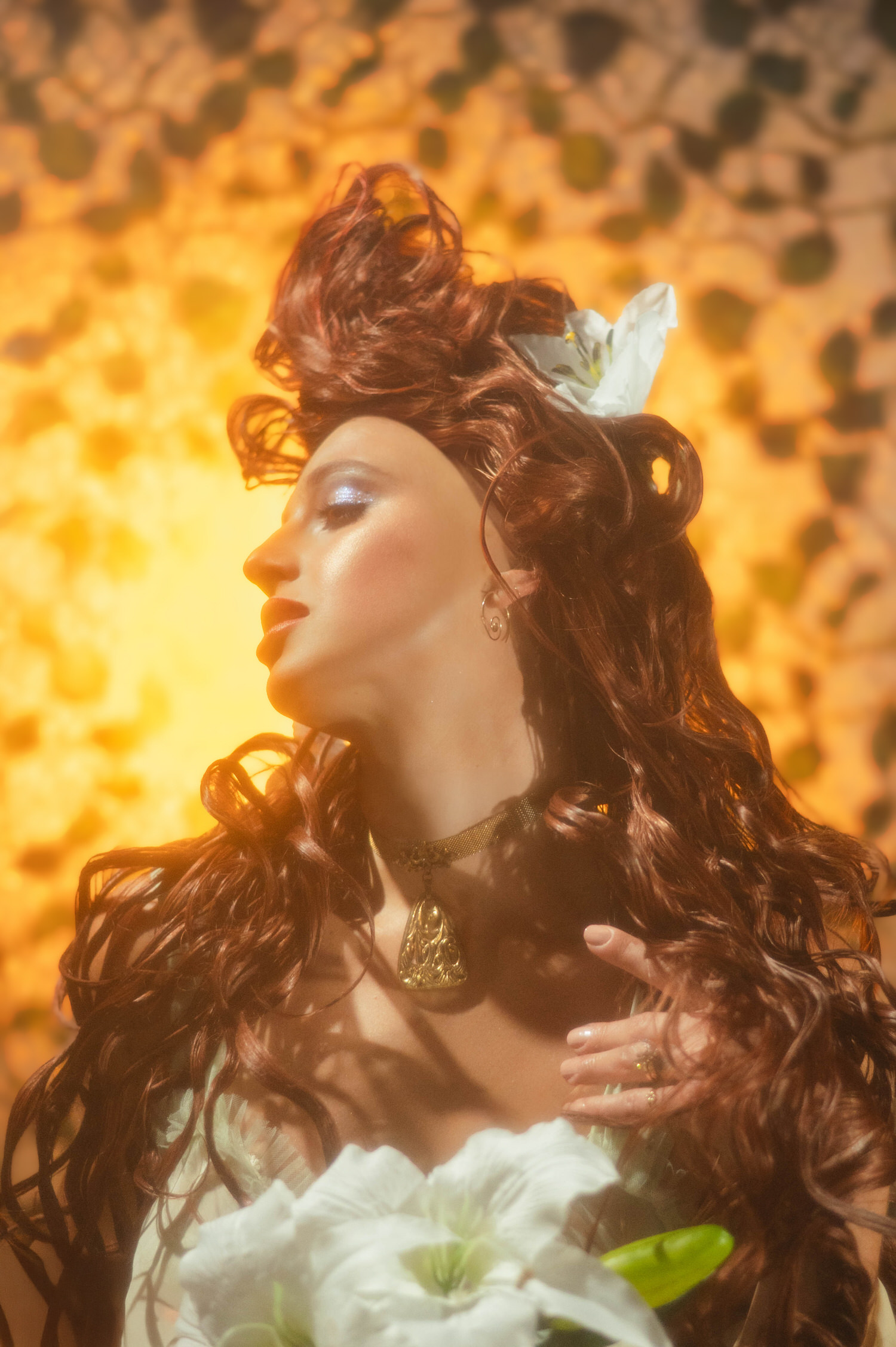 Soft focus Art Nouveau inspiration photography. Moody portrait of a woman with white lilies and an elegant updo against a green ivy-patterned screen.