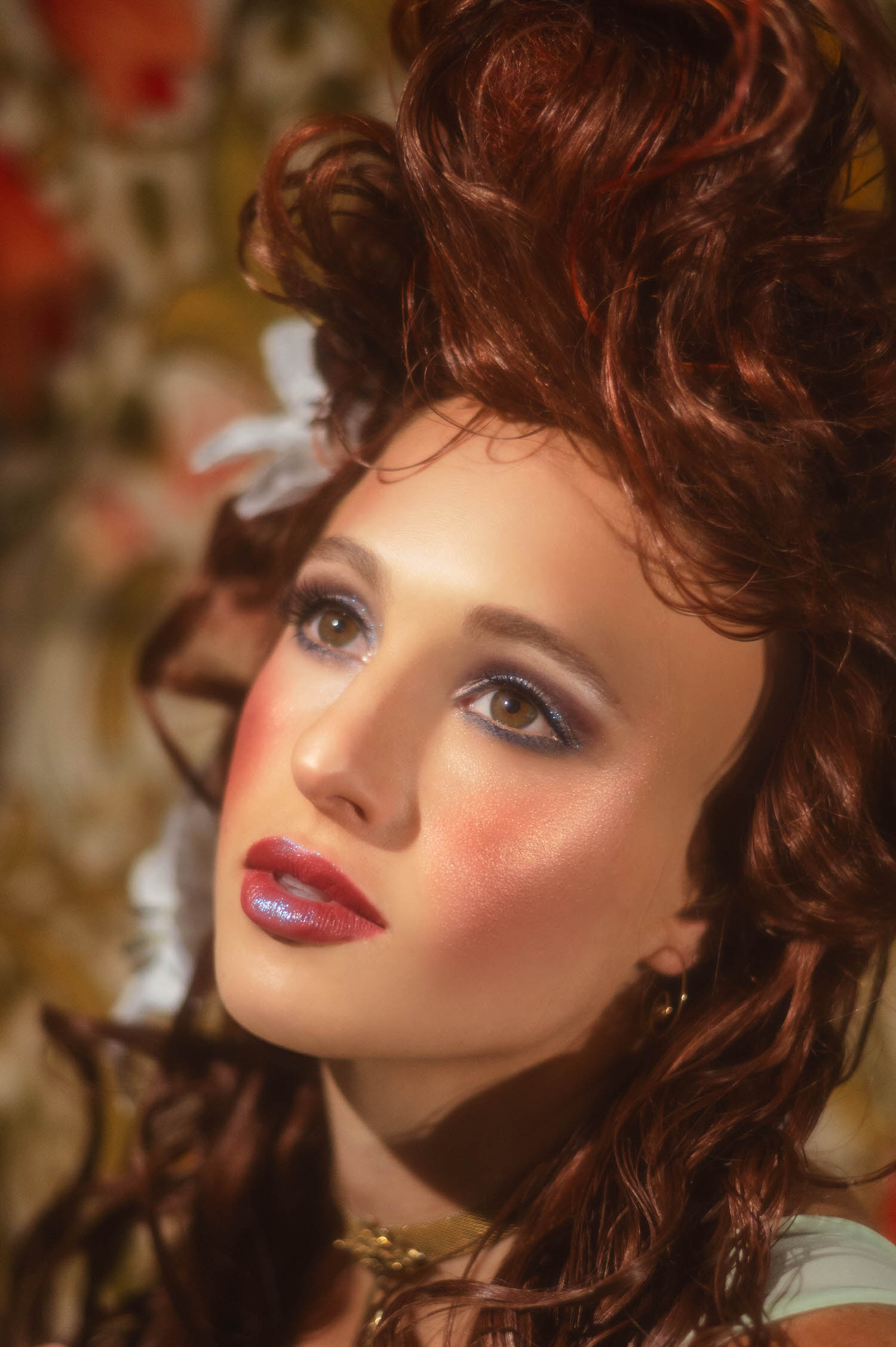 Close-up beauty shot capturing Art Nouveau inspiration. Shimmering eyeshadow, bold blush, and classic updo with white lilies for an ethereal vintage aesthetic.