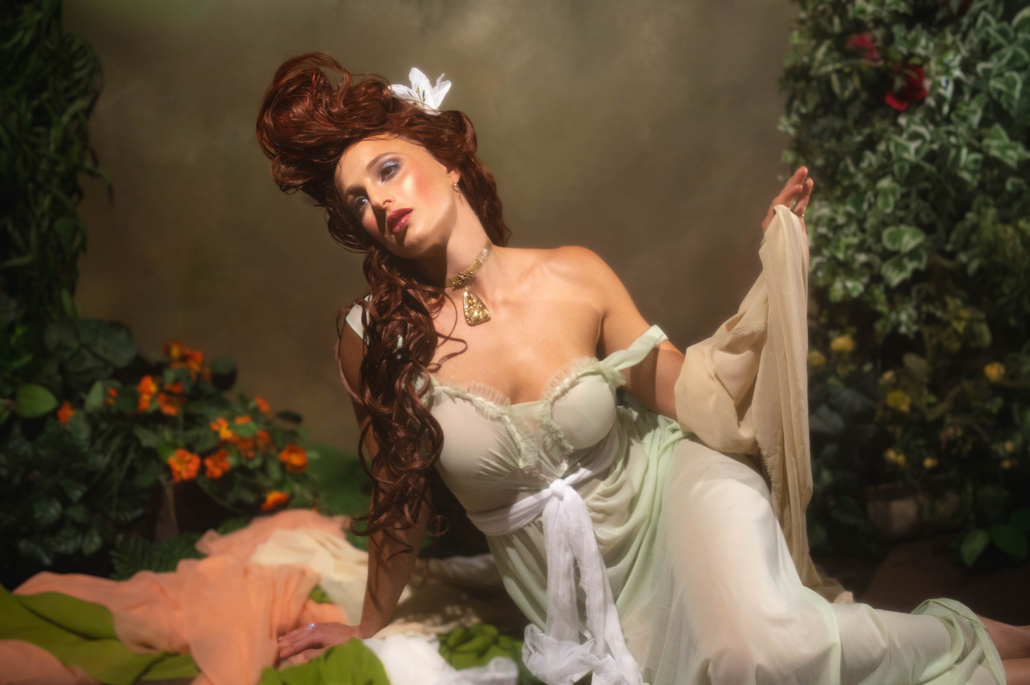An Art Nouveau photoshoot at Royal Lune Studio in the Dallas area. A model with an elaborate red hairdo reclines on fabrics, showcasing a classic fine art look.