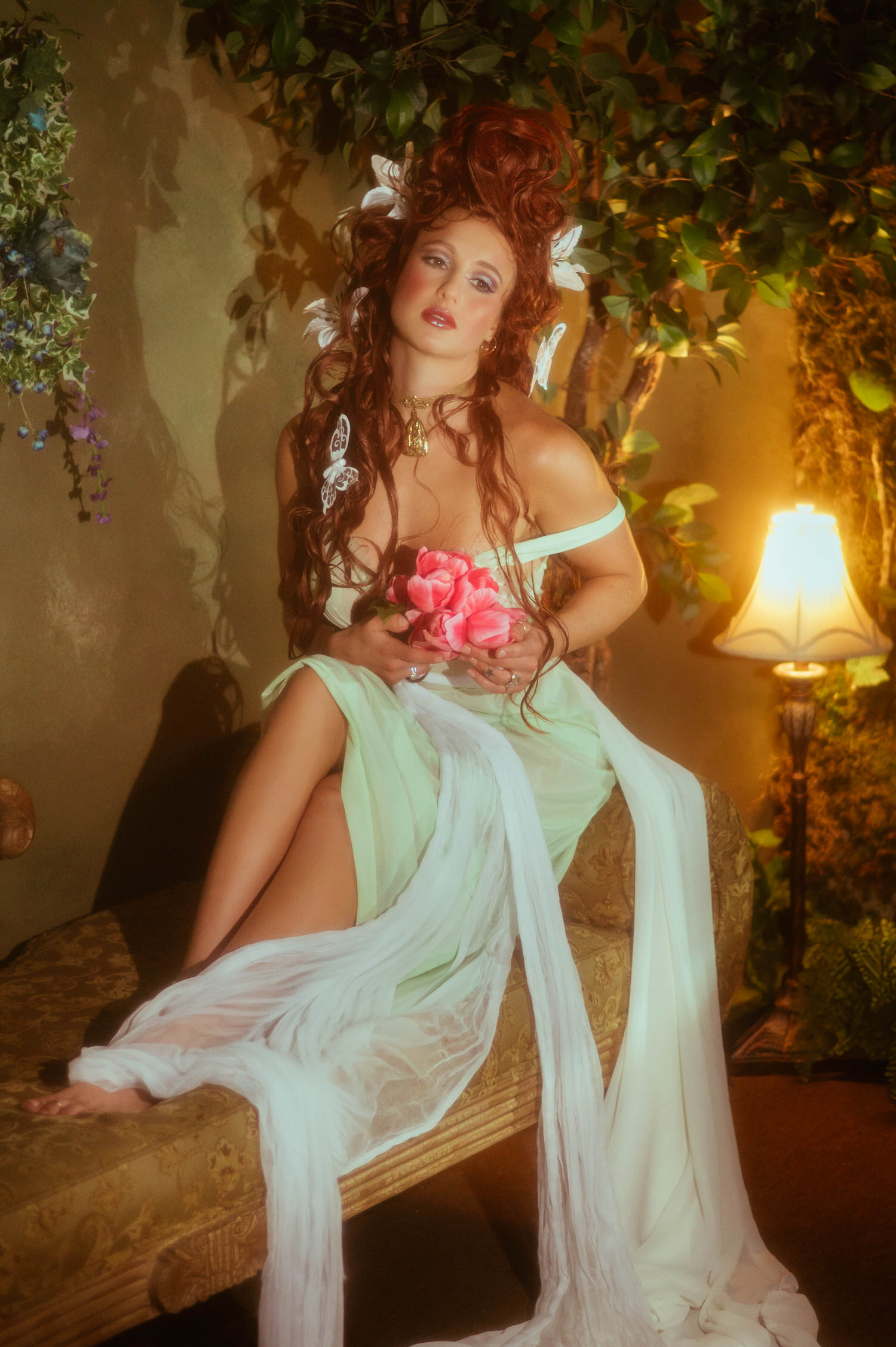 A model in a sage green vintage dress strikes an expressive pose on a vintage couch at Royal Lune Studio. This portrait embodies romantic Art Nouveau style elements.