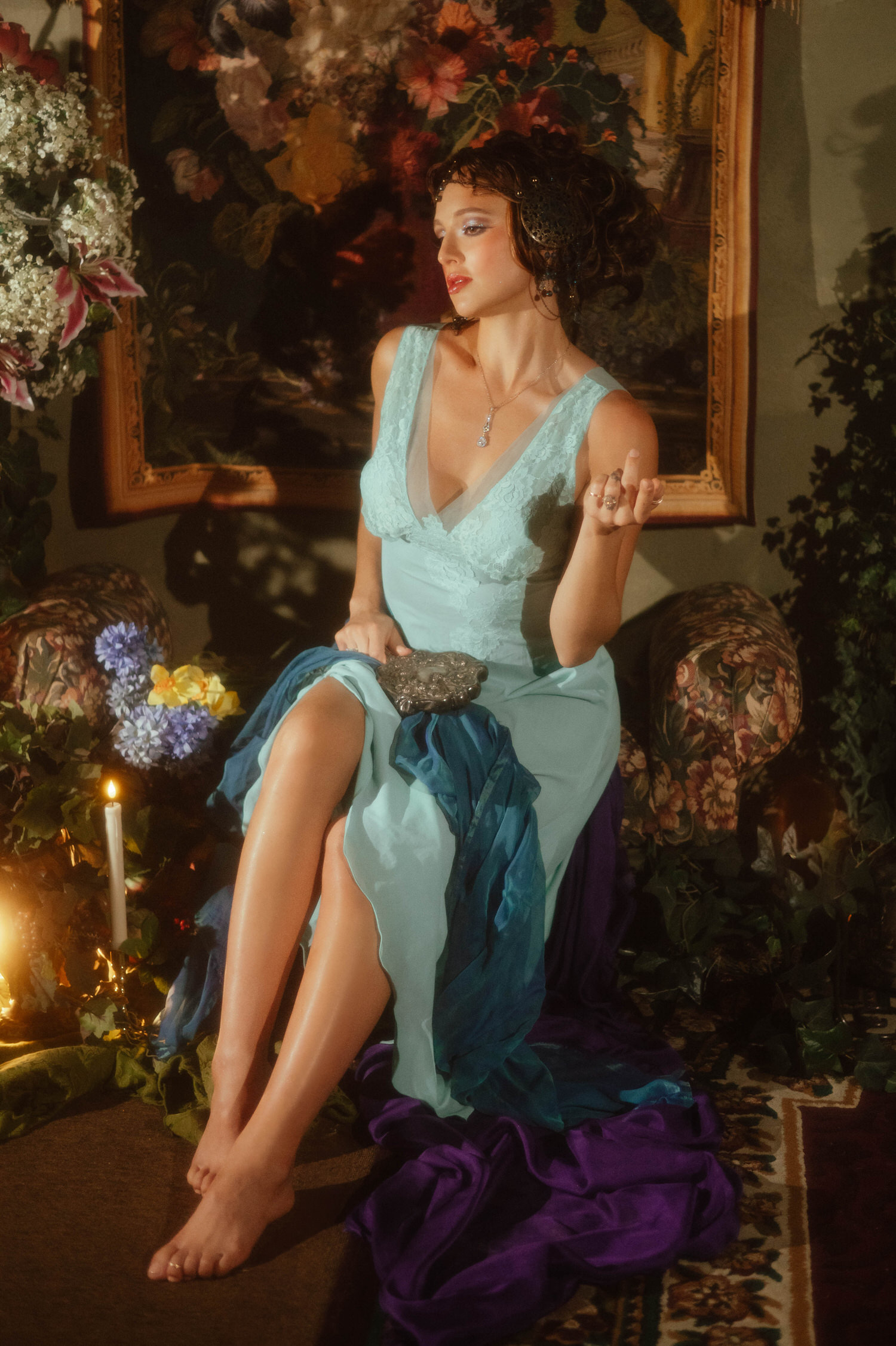 Fine art portrait showcasing Art Nouveau inspiration. A woman in a light blue gown is seated on a vintage sofa in front of a large floral tapestry.