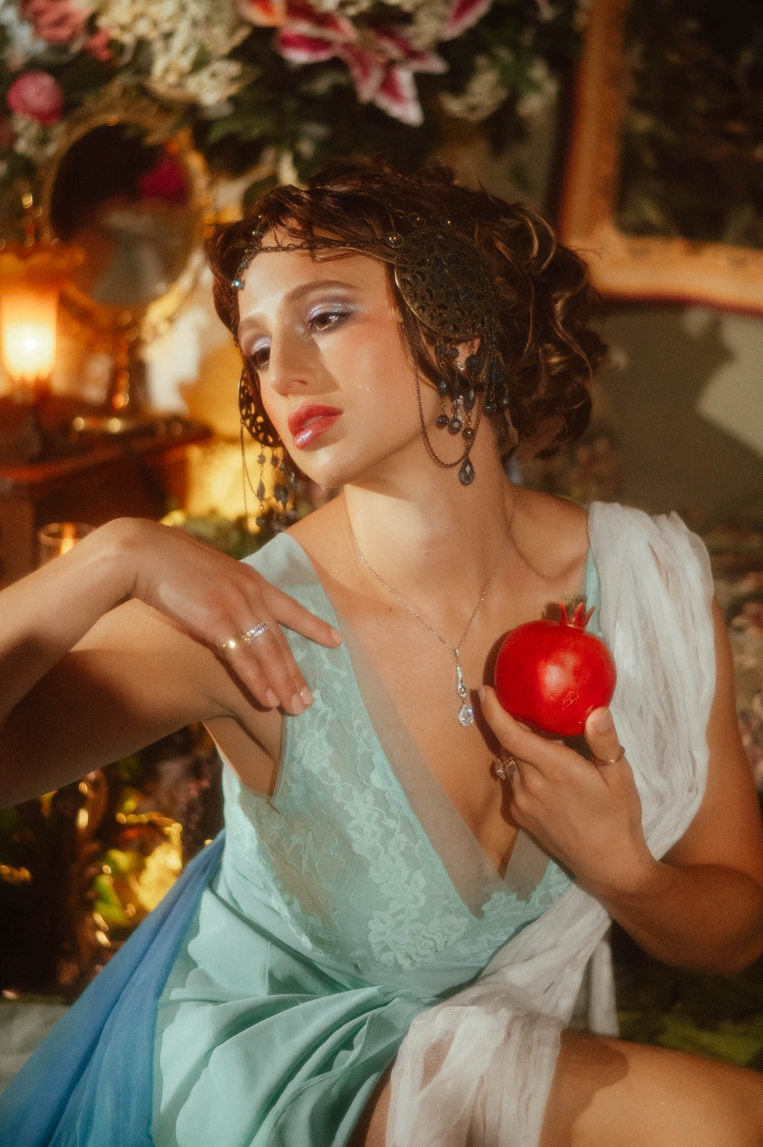 An ethereal Art Nouveau photoshoot close-up. The model poses with a red pomegranate while wearing a decorative bronze hair ornament at Royal Lune Studio.