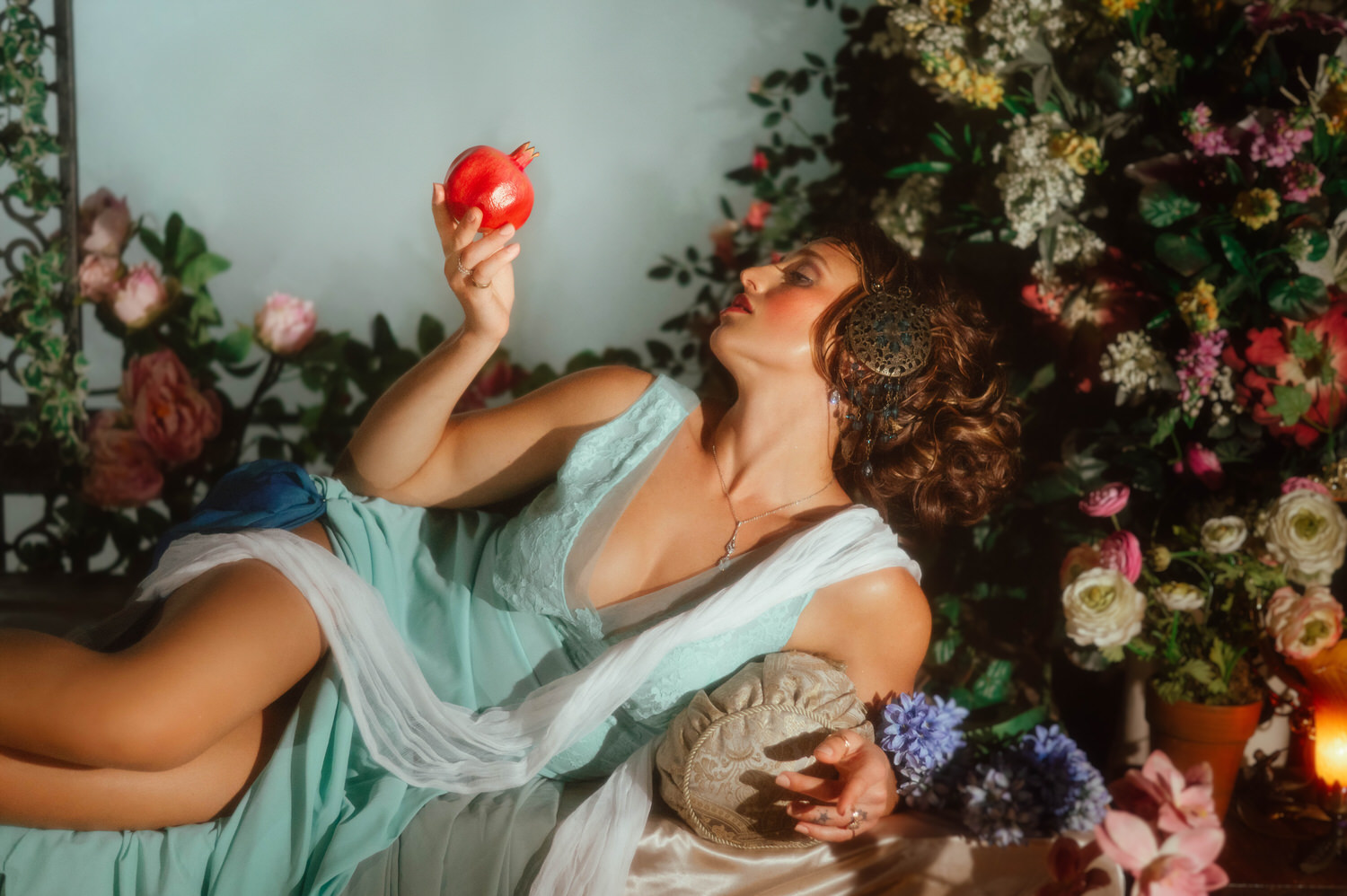 A model displays elegant Art Nouveau style during a fine art session. She reclines on a silk-draped surface surrounded by colorful floral arrangements.