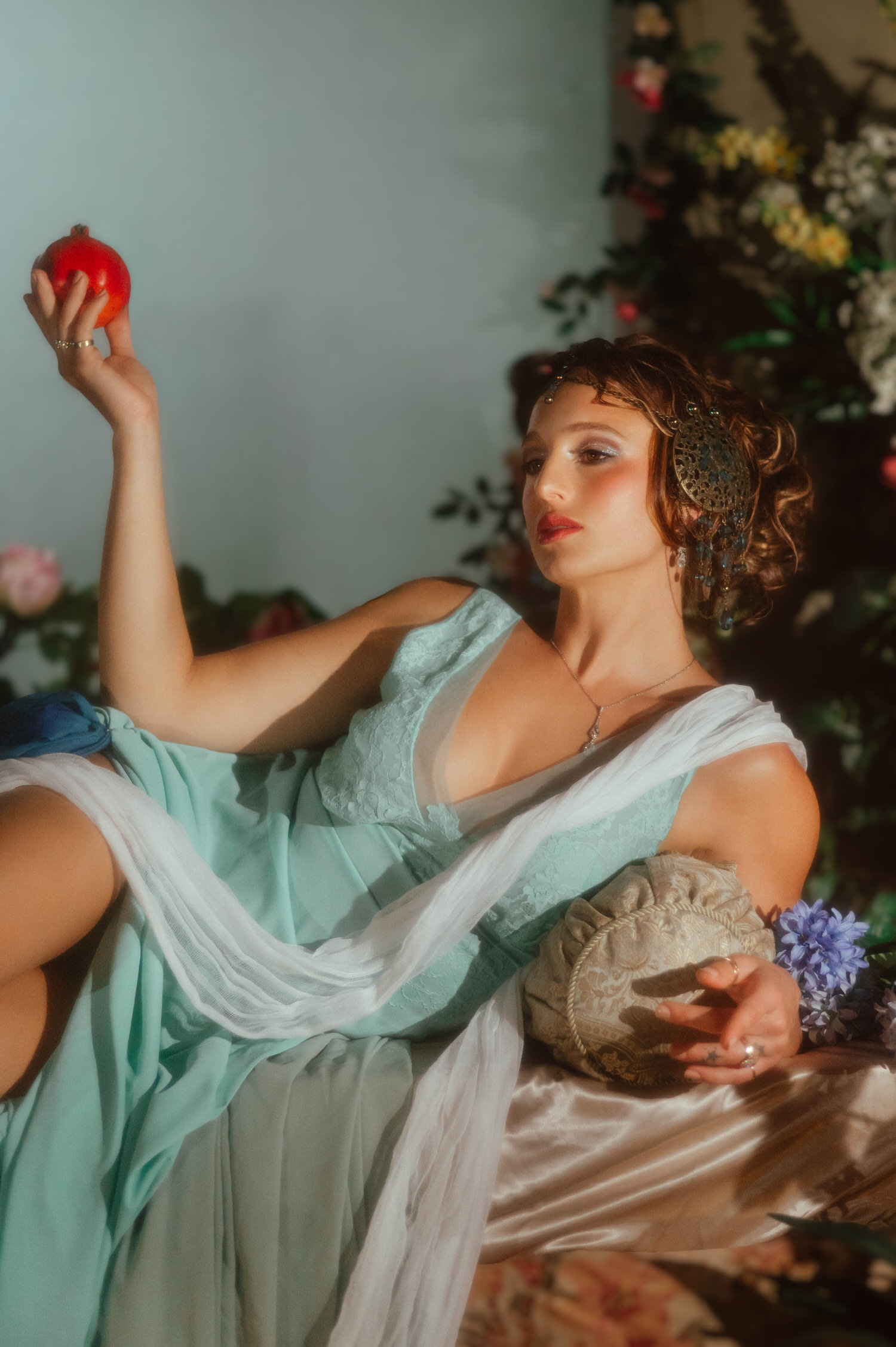 Art Nouveau inspiration captured in a Dallas area studio. A reclining model wears a blue dress and holds a pomegranate aloft at Royal Lune Studio.