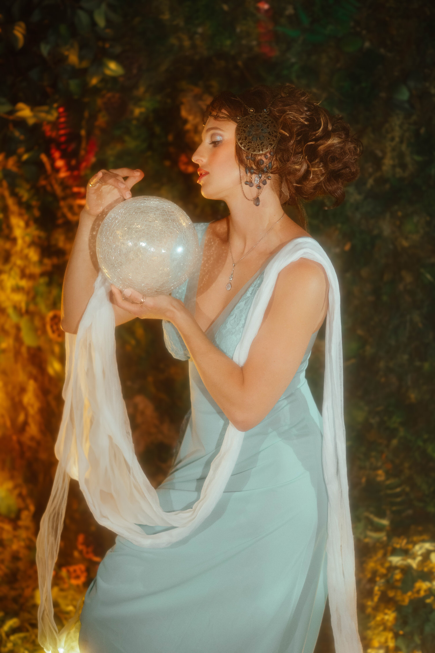 An elegant Art Nouveau photoshoot image. The model holds a glowing glass sphere wrapped in a white chiffon sash under warm studio lighting.
