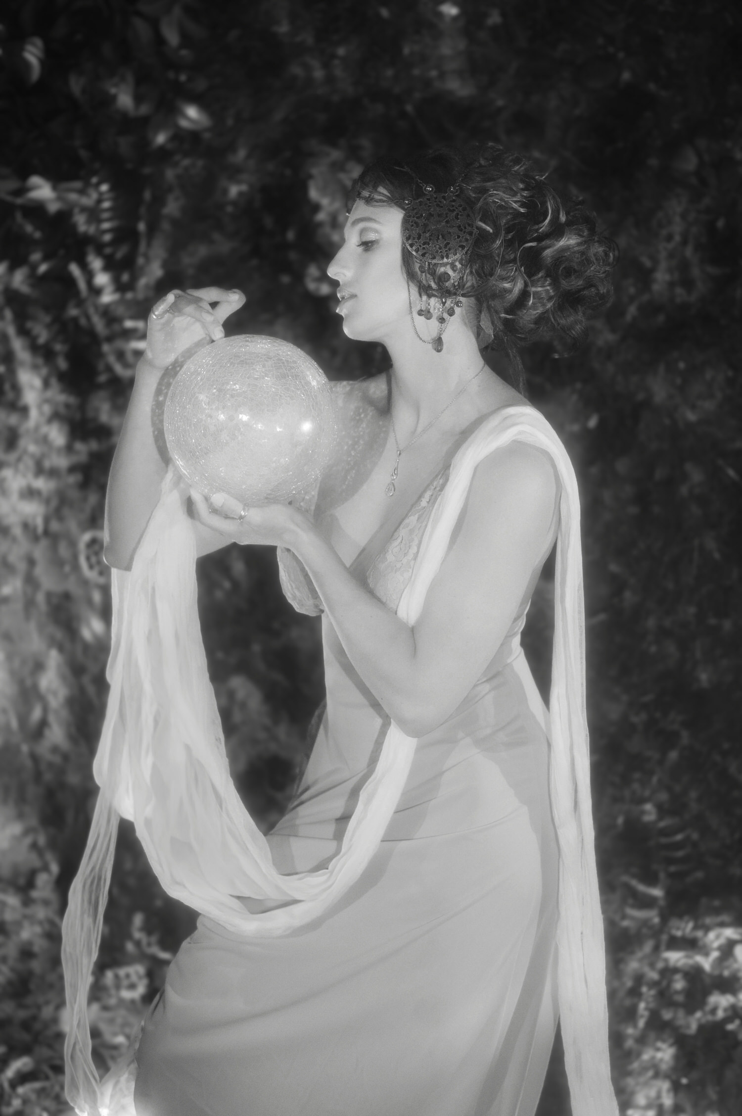 Black and white Art Nouveau photoshoot image from Royal Lune Studio in the Dallas area. A model in a draped gown gazes at a glowing glass sphere.
