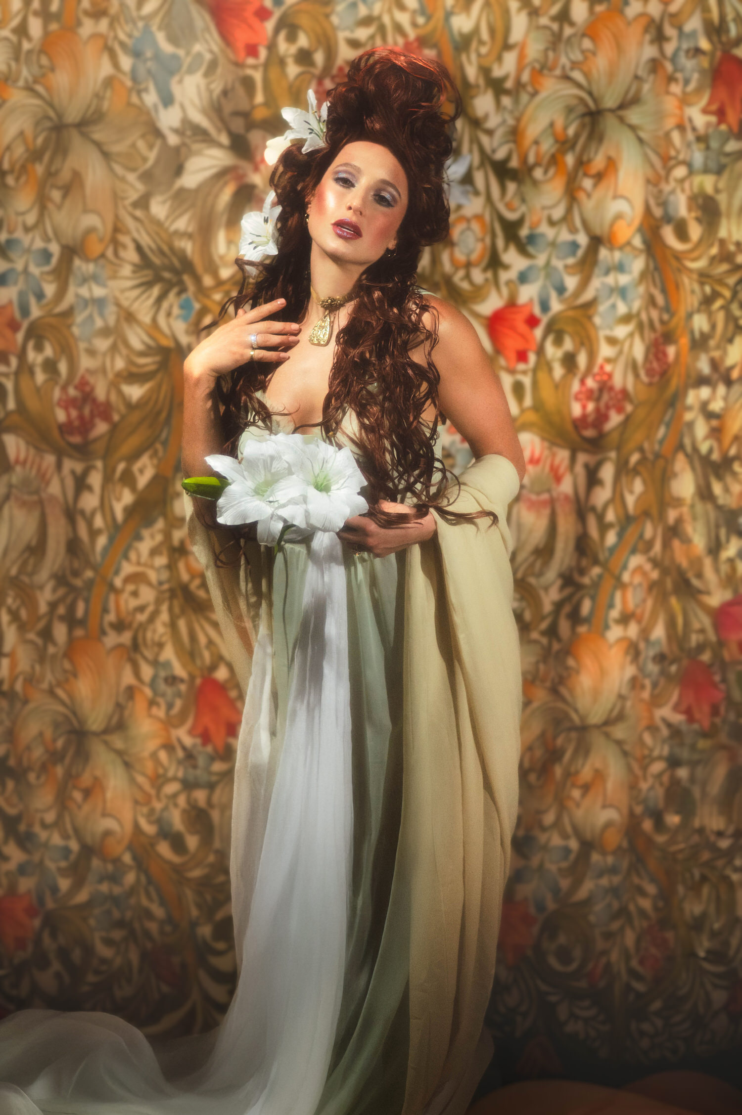 Art Nouveau inspiration editorial portrait. Redhead model in ethereal flowing drapery holding white lily blossoms, reminiscent of Alphonse Mucha paintings.