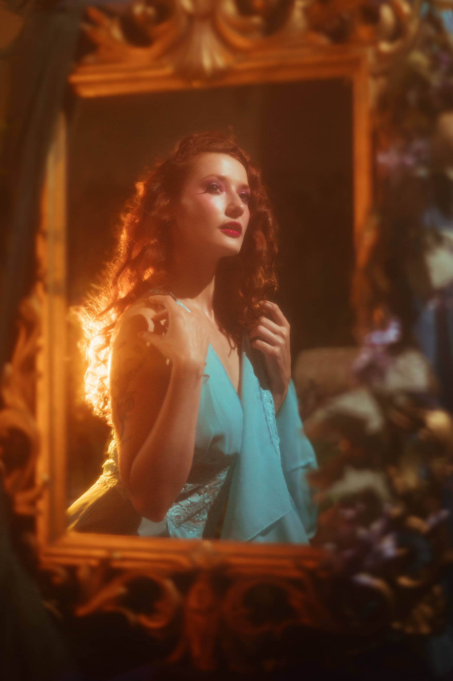 A model in a vintage lace nightgown poses within an ornate gold mirror frame, glowing in warm light for a fine art Midsummer Night's Dream photoshoot. This dreamy photography studio image was created near Dallas. Royal Lune Photo.