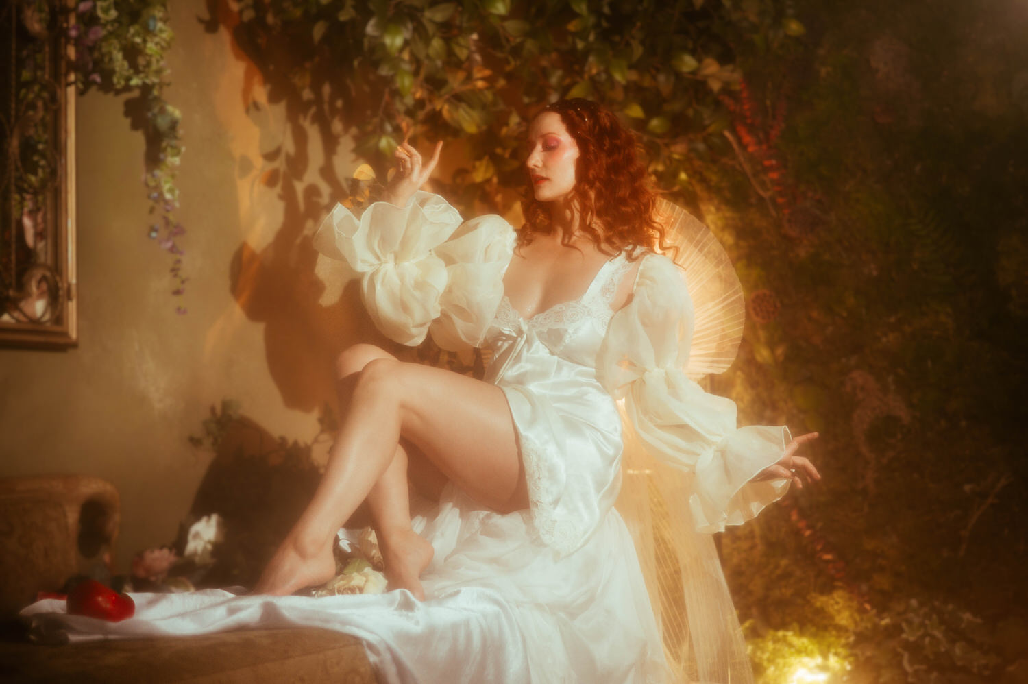 A model in a flowing white vintage nightgown with voluminous sleeves sits among golden light and an ornate fan, reflecting the fine art aesthetic of a Midsummer Night's Dream photoshoot. This dreamy photography studio image was captured near Dallas. Royal Lune Photo.