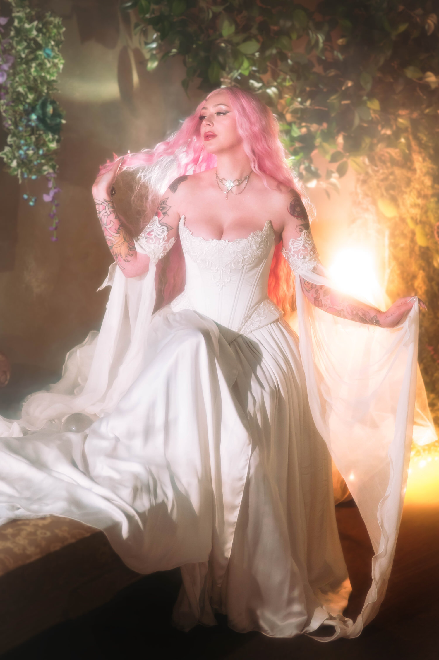Bride posing with draped sheer sleeves in a structured fantasy bridal gown, surrounded by ivy and warm backlight for renaissance fair wedding photography.