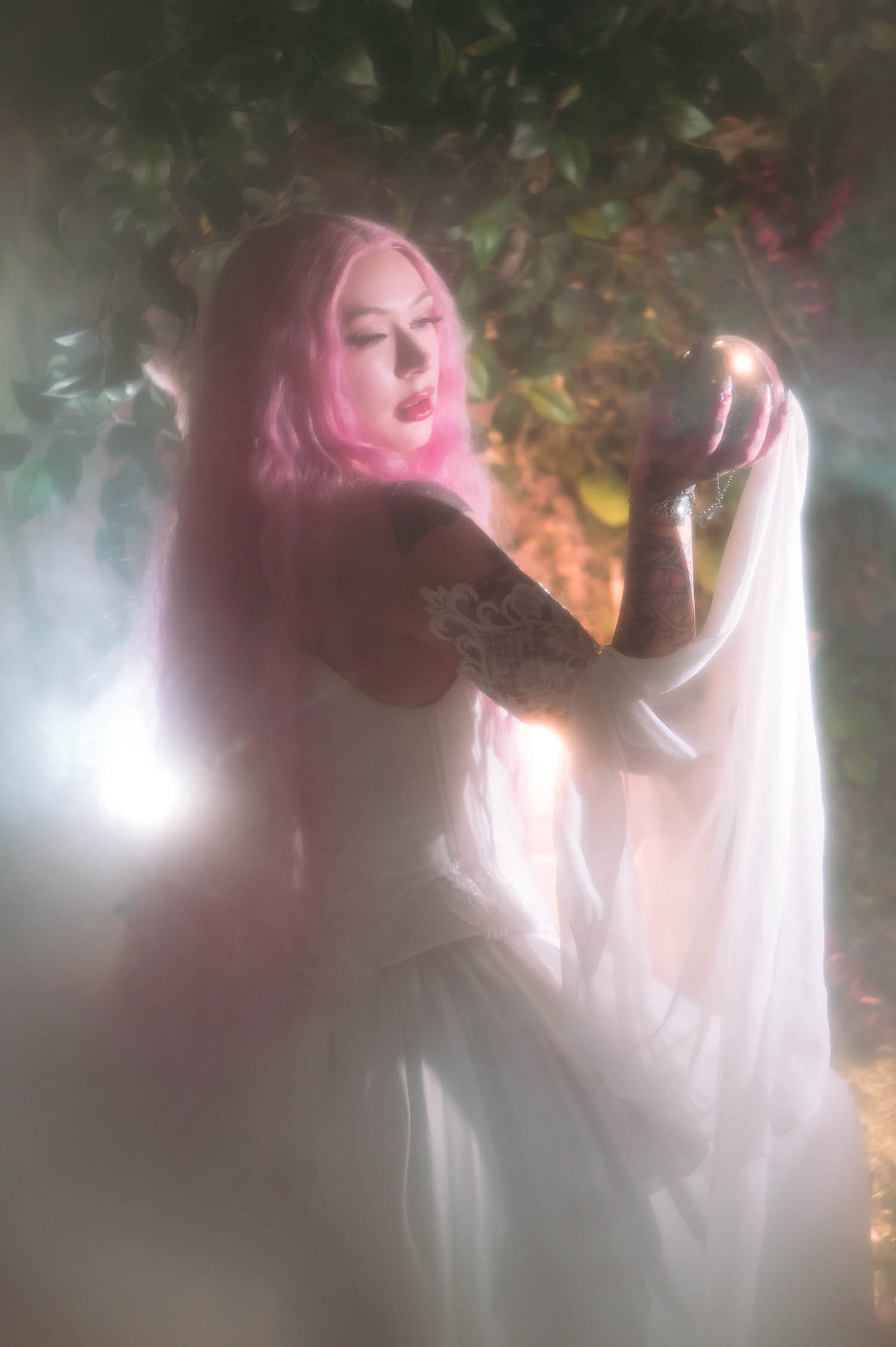 Side profile of bride holding a glass orb prop in a fantasy bridal photos session, showcasing delicate lace sleeve details and flowing fabric.